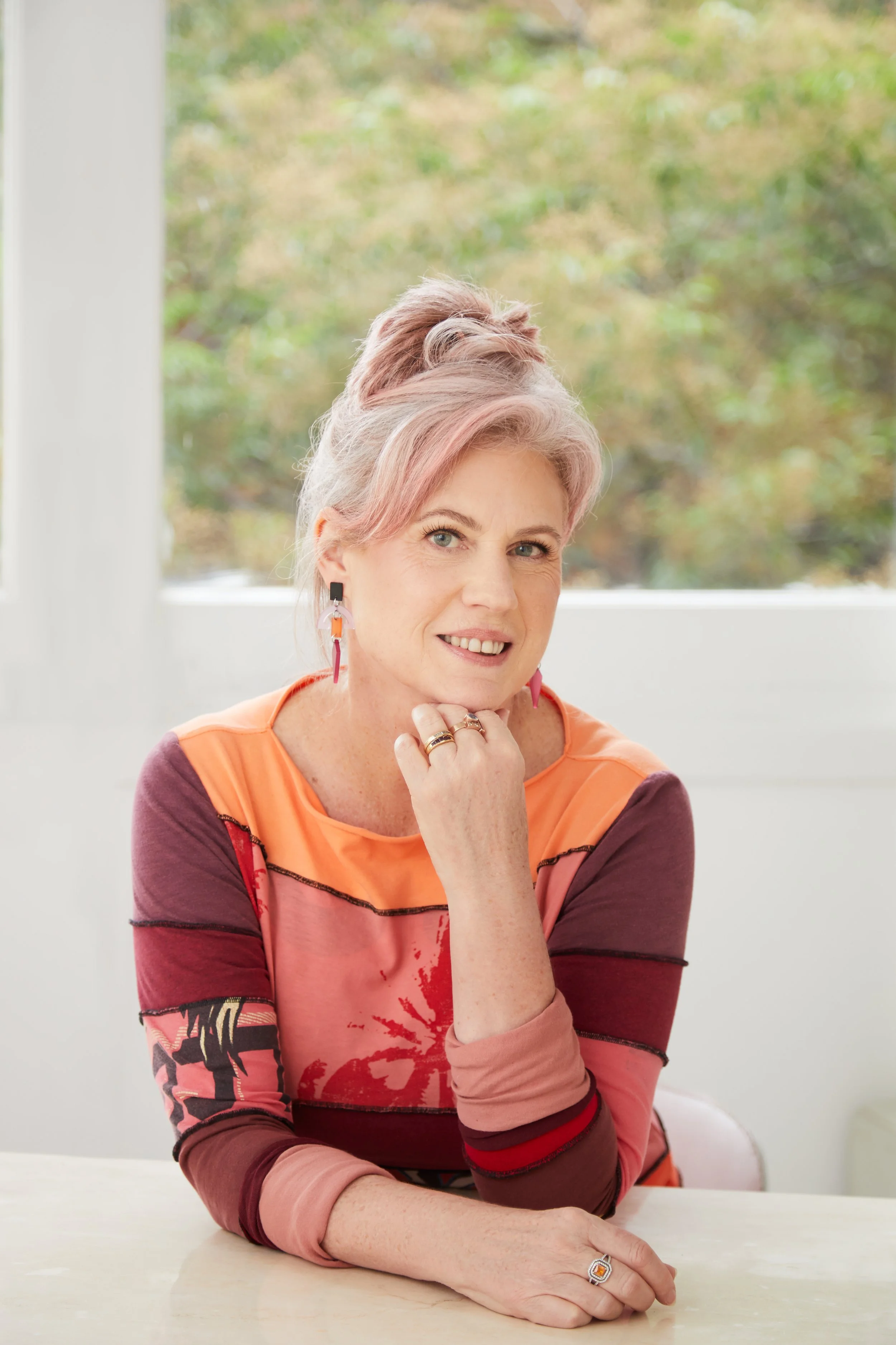 Donna in a multi-coloured dress sitting at a table looking directly ahead and smiling
