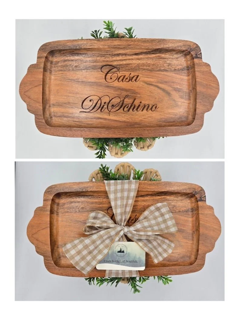 A wooden tray with the words 'Casa DiSchino' engraved on the inside, decorated with green plants, and tied with a beige checkered ribbon and a small tag.