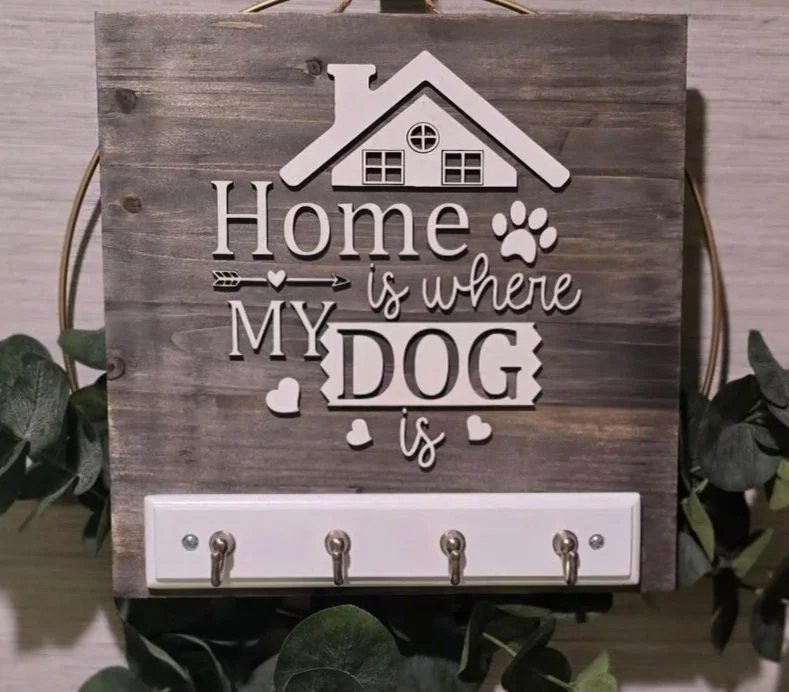 Wooden wall decor with the quote 'Home is where MY DOG is' and hooks for keys or leashes, surrounded by a green wreath.