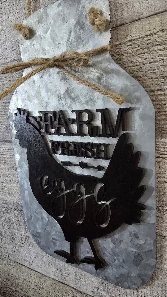 Decorative metal wall art featuring a chicken silhouette with the words "Farm Fresh Eggs" inside, hanging from a jute twine on a textured wall.