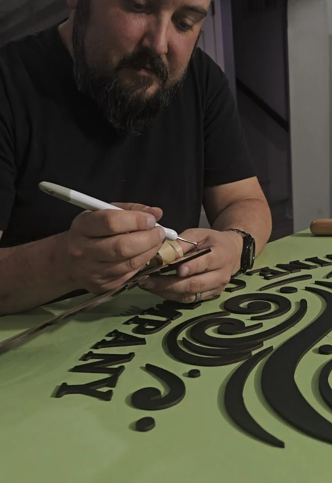 A man with a beard adding finishing touches to a custom business sign for a dog daycare in an indoor setting.