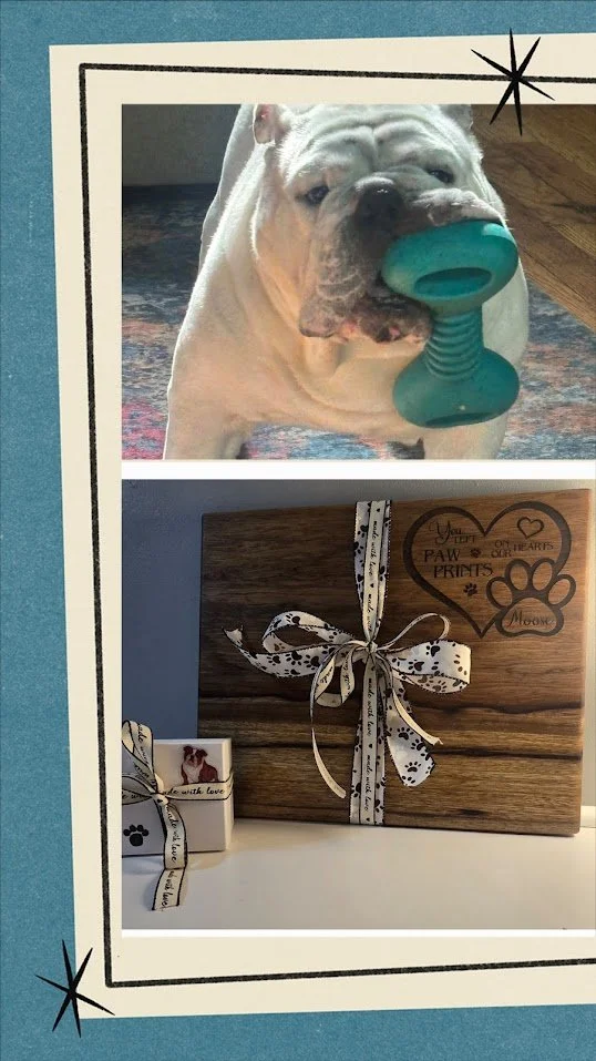 A dog holding a teal rubber toy in its mouth and a wooden cutting board with a patterned ribbon and a small gift box with a photo of a dog on it. Pet memorial gift.