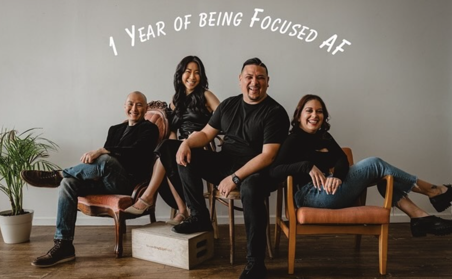 Four diverse people sitting and lying on chairs in a room with a potted plant, smiling, with the text '1 Year of Being Focused AF' above them.