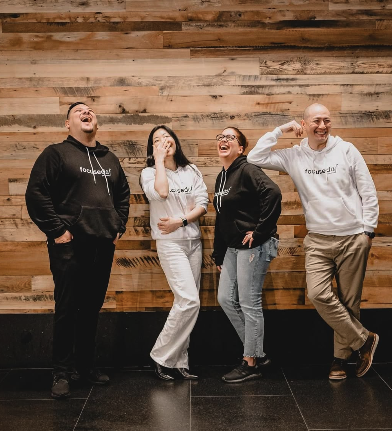 Four people standing in front of a wooden wall, laughing and smiling, wearing hoodies with the 'focusedaf' logo.