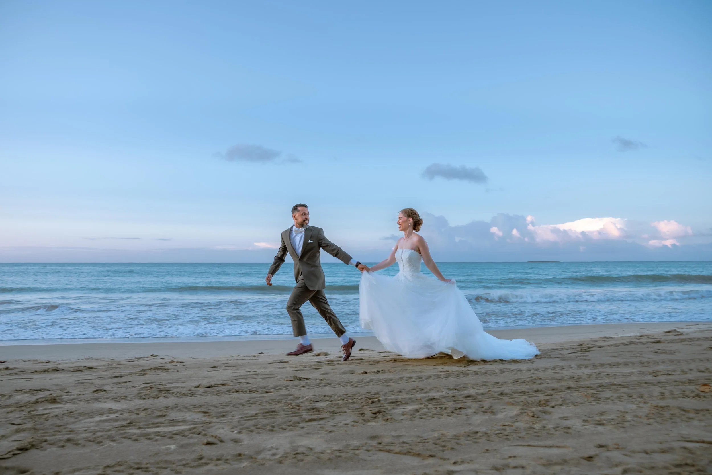 A bride and groom holding hands and walking on the beach during sunset in Puerto Rico.