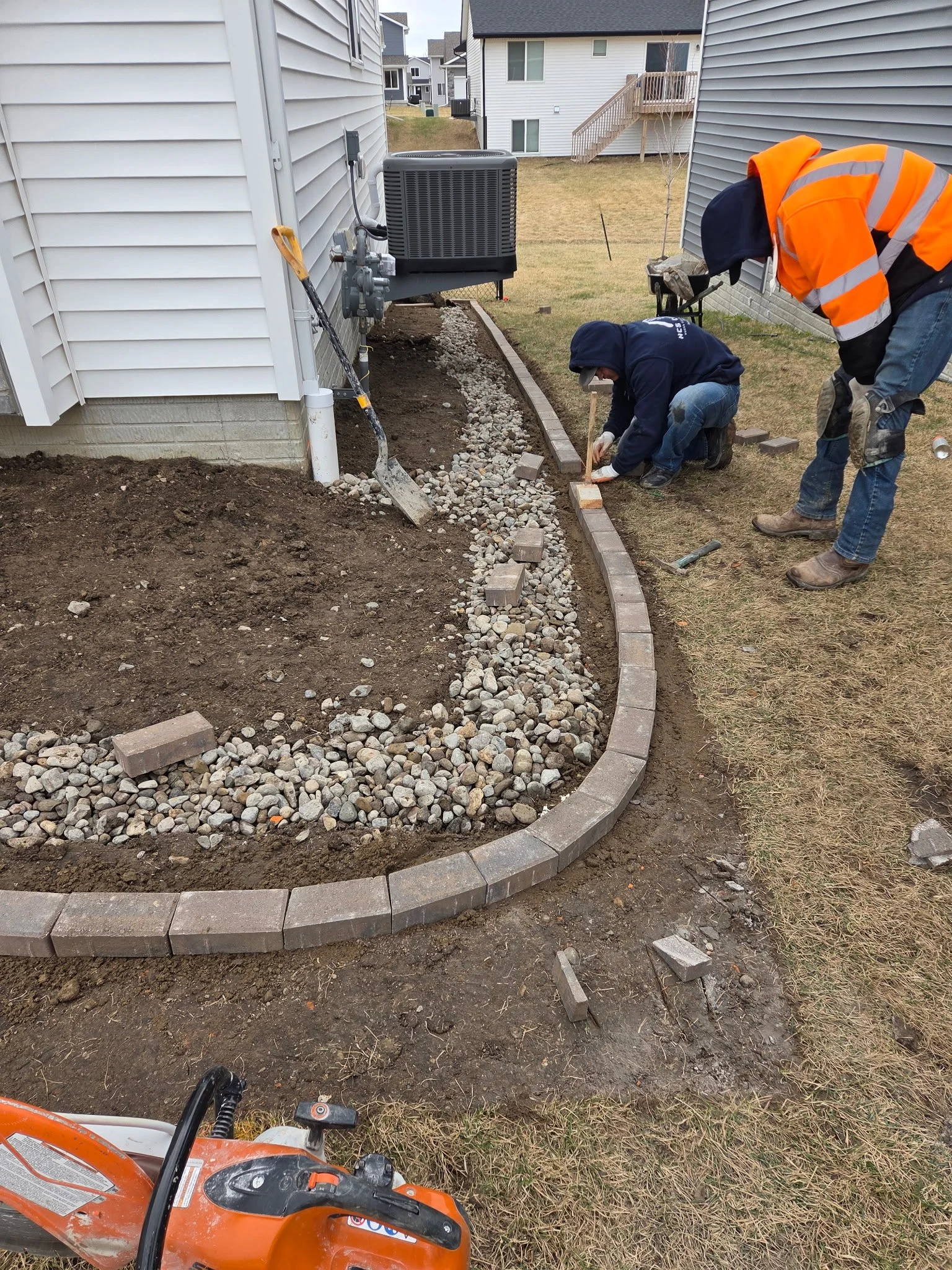 HCS crew precisely laying decorative block edging for a custom hardscape rock bed next to the home.