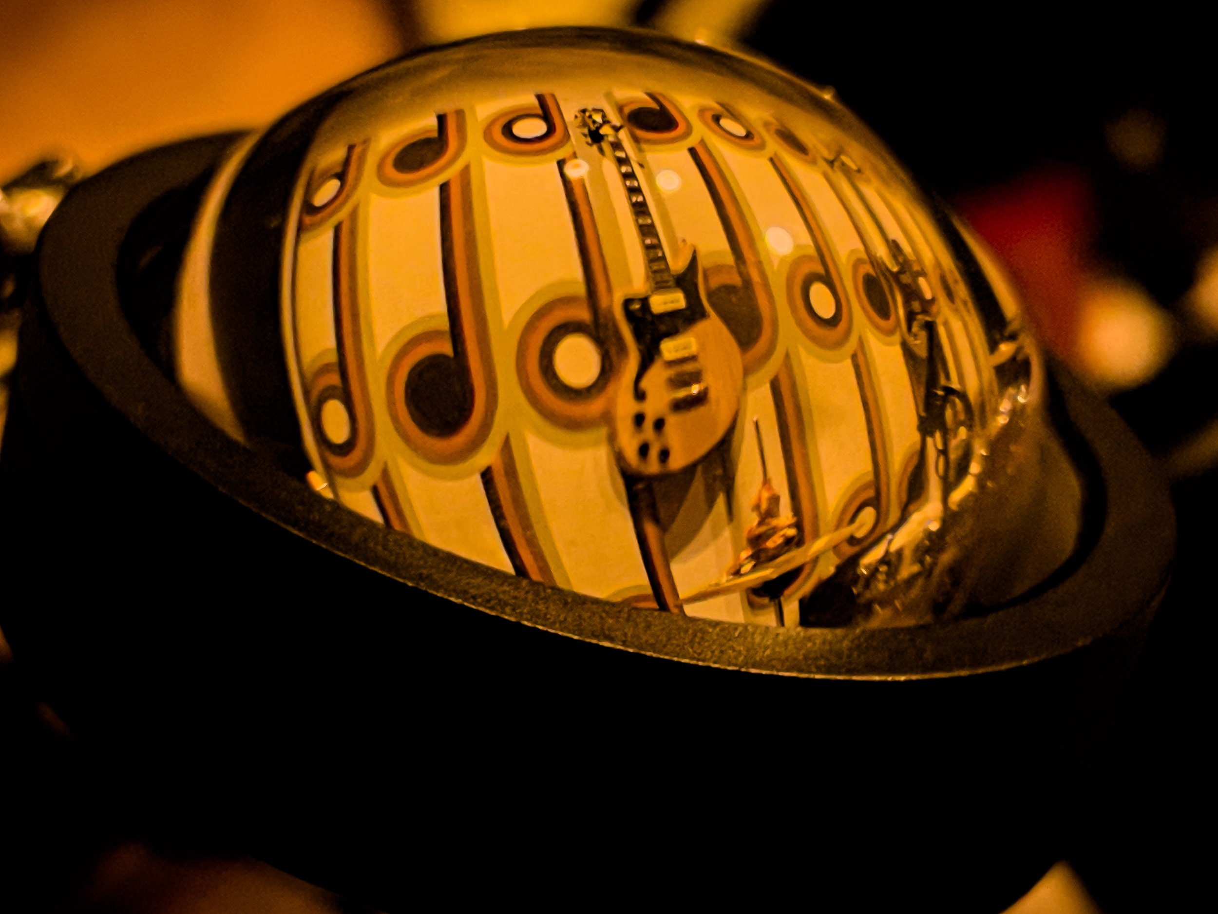 Close-up of a vintage-style clock with a rounded glass dome, displaying the time with black hands, surrounded by orange and yellow decorative patterns, set against a dark background.