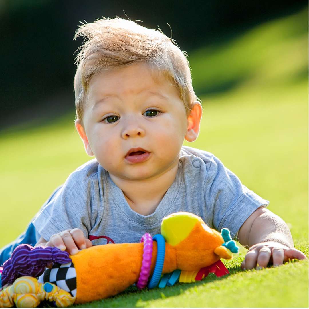 kelowna infant boy sitting on grass with plush toy daycare