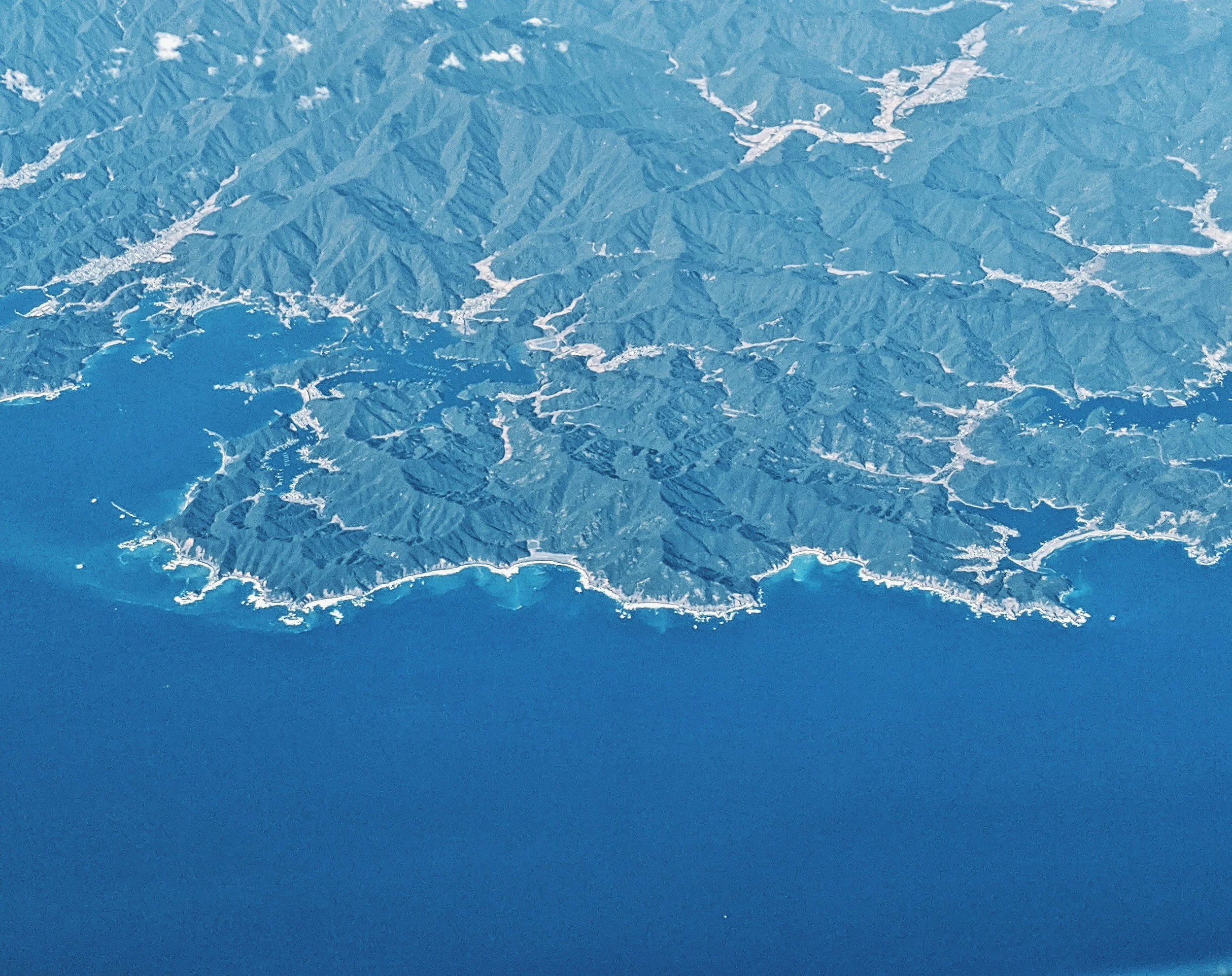 海に面した山岳地帯の上空からの空撮写真。山々が連なる自然の風景が広がる。