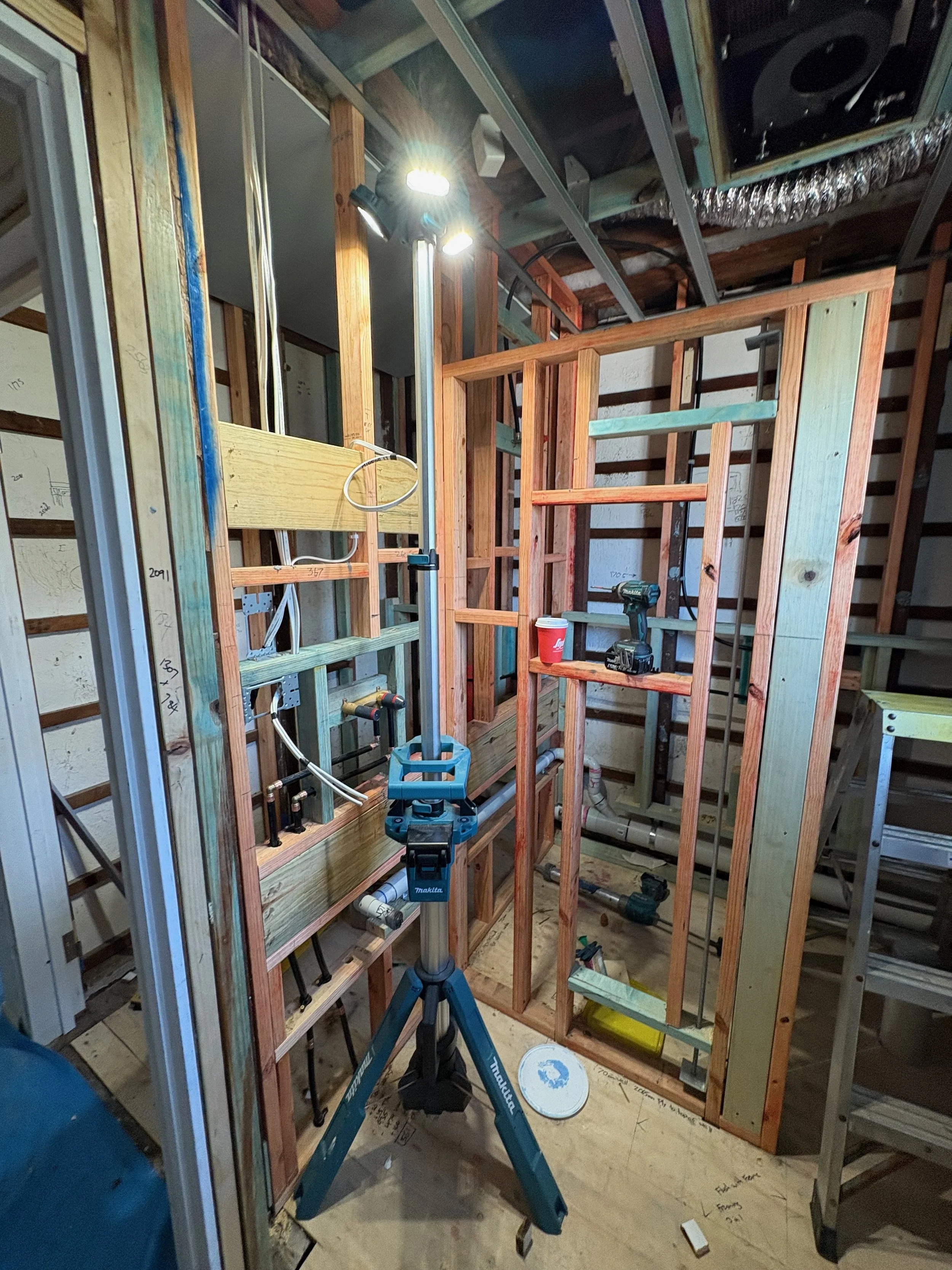 Construction site with wooden framing and tools, including a drill and a portable work light.