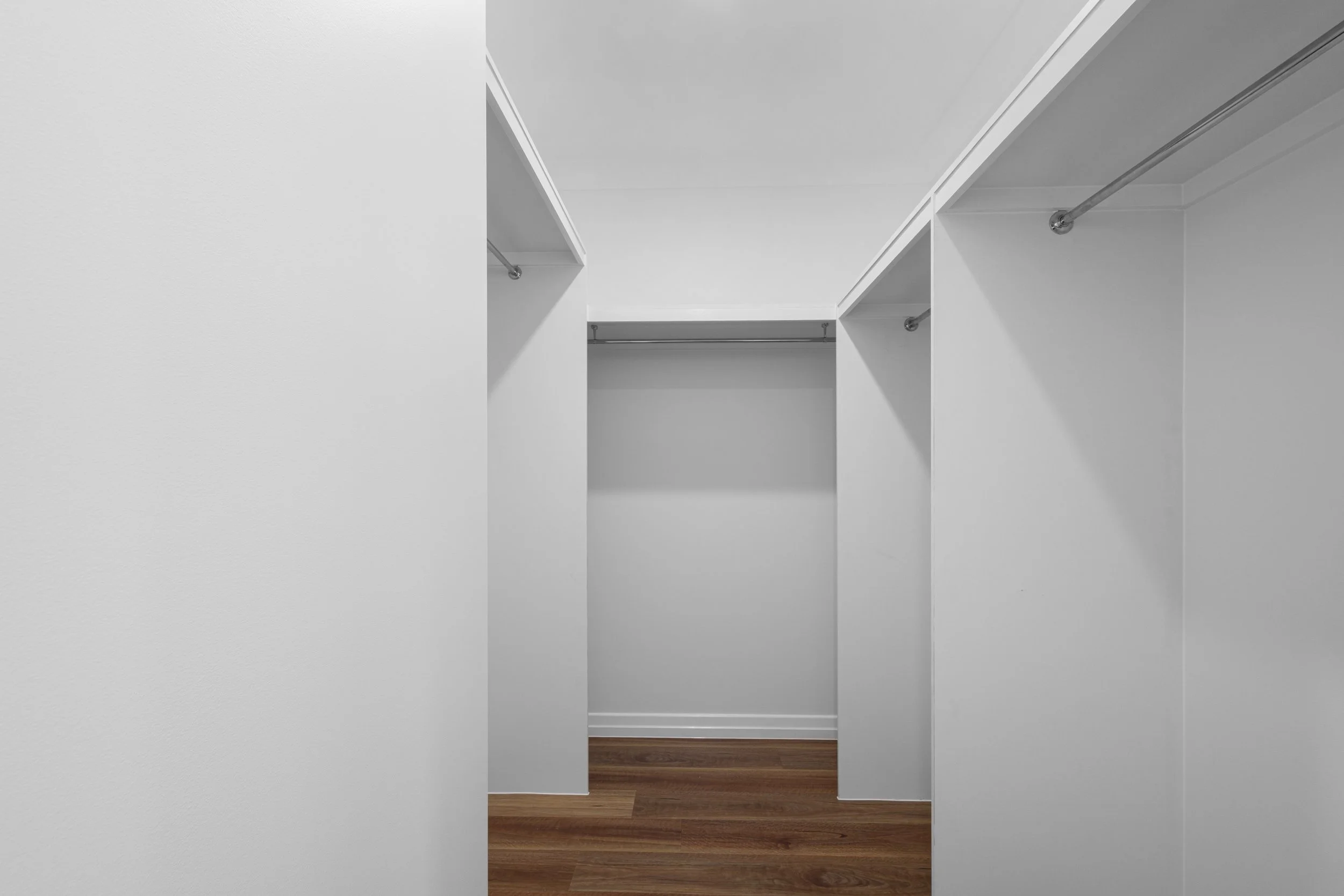 Empty walk-in closet with white walls, ceiling, and shelves, and a hardwood floor.