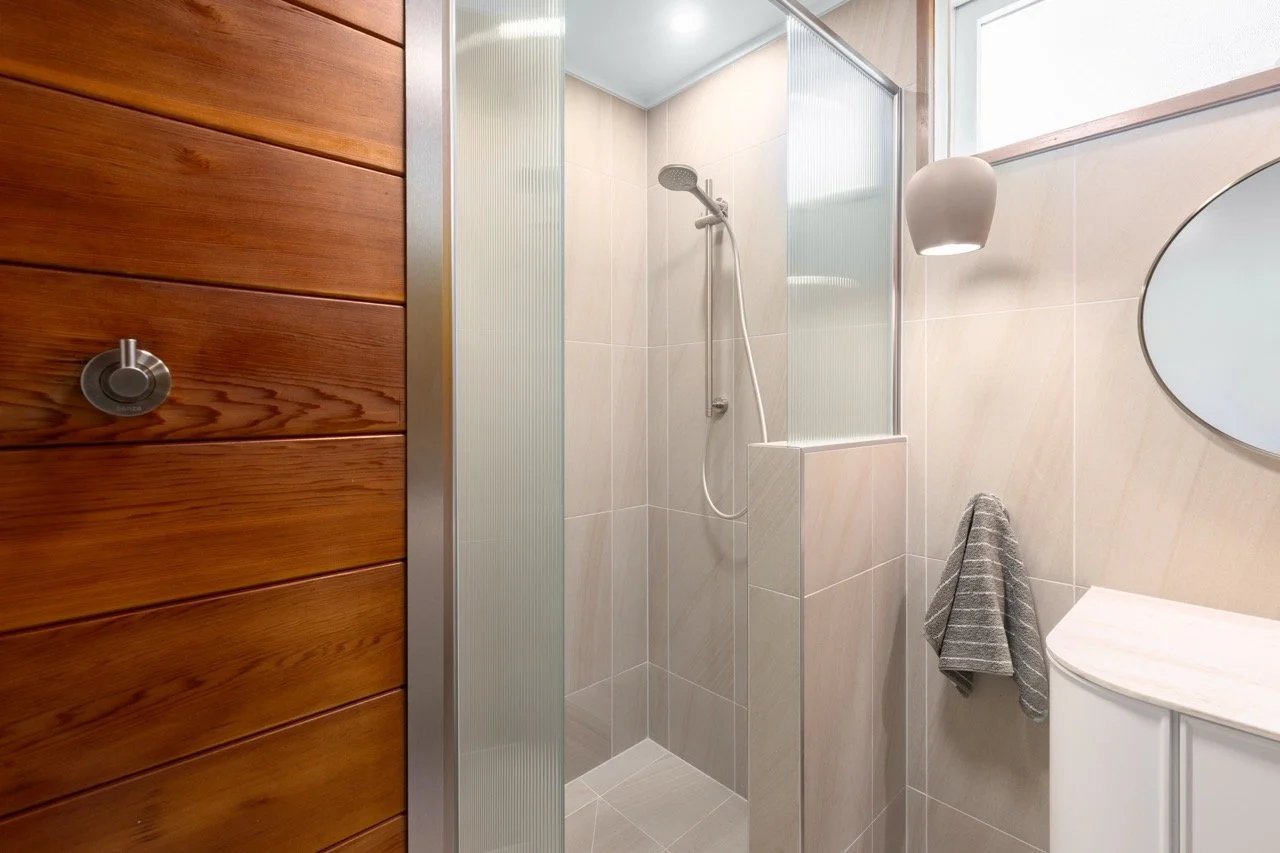 Small modern bathroom with a walk-in shower, a gray towel hanging on a hook, a white vanity with a marble top, a mirror, and a potted plant hanging from the ceiling.