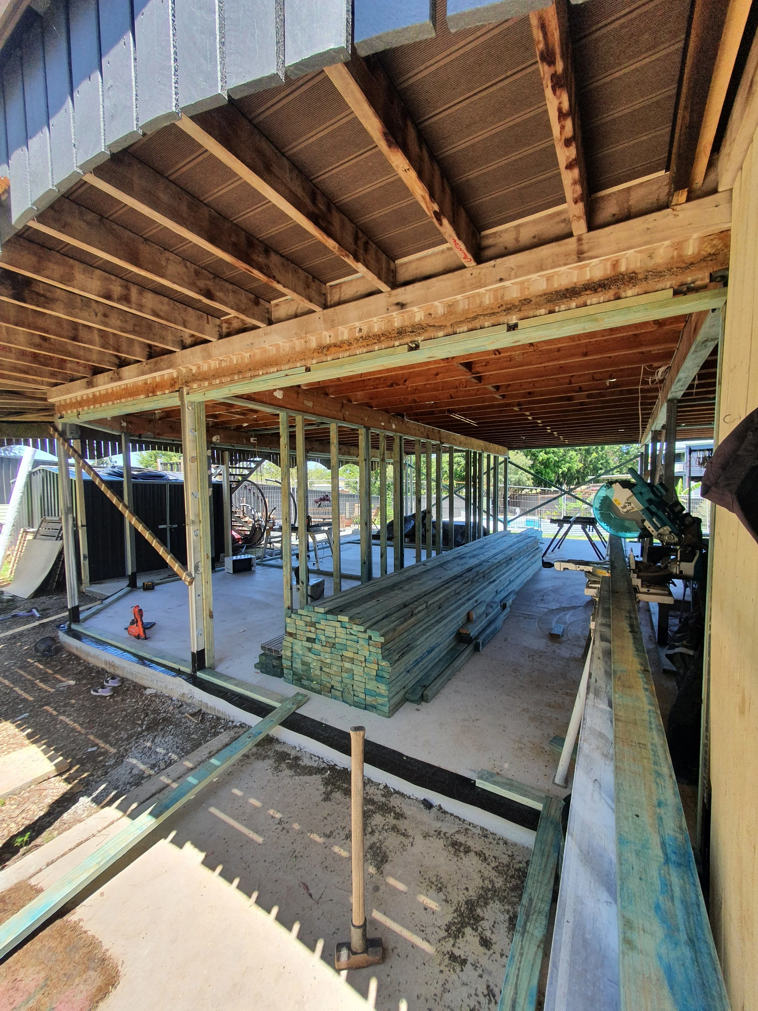 Construction site with wooden framing and stacked green lumber inside a partially built structure.