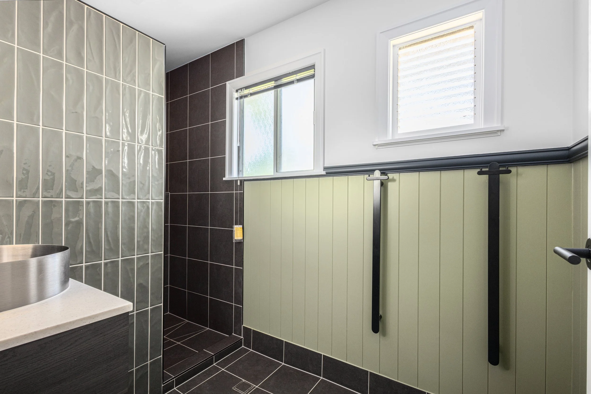 Bathroom with green beadboard wainscoting, black hooks on the wall, frosted windows, and a glass block shower wall.