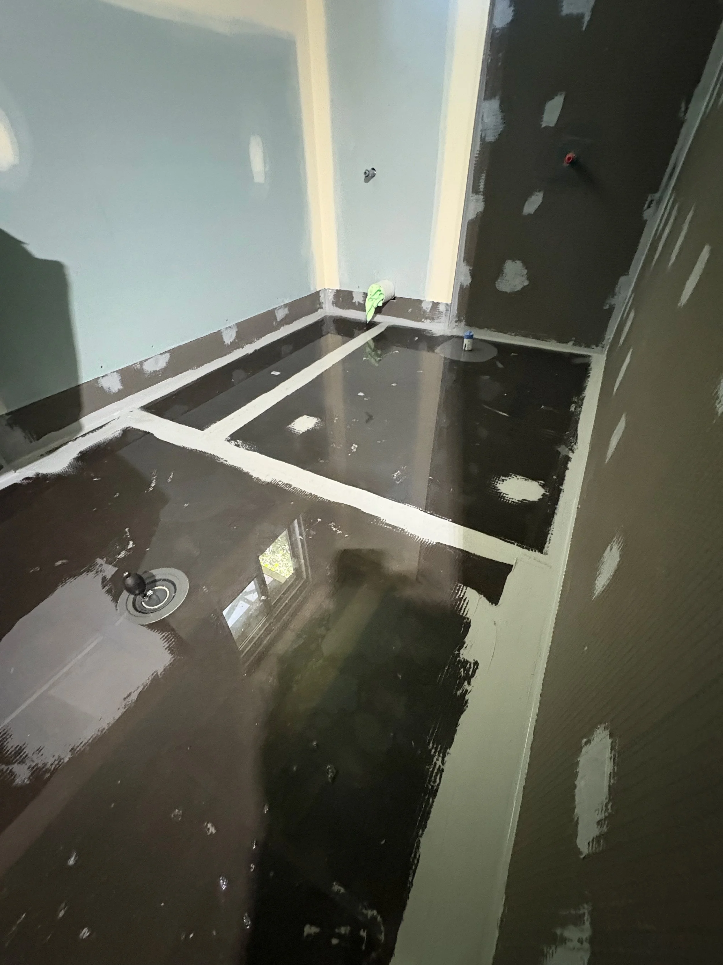 Room under construction with black glossy flooring, partially painted walls, and exposed drywall with drywall mud patches.