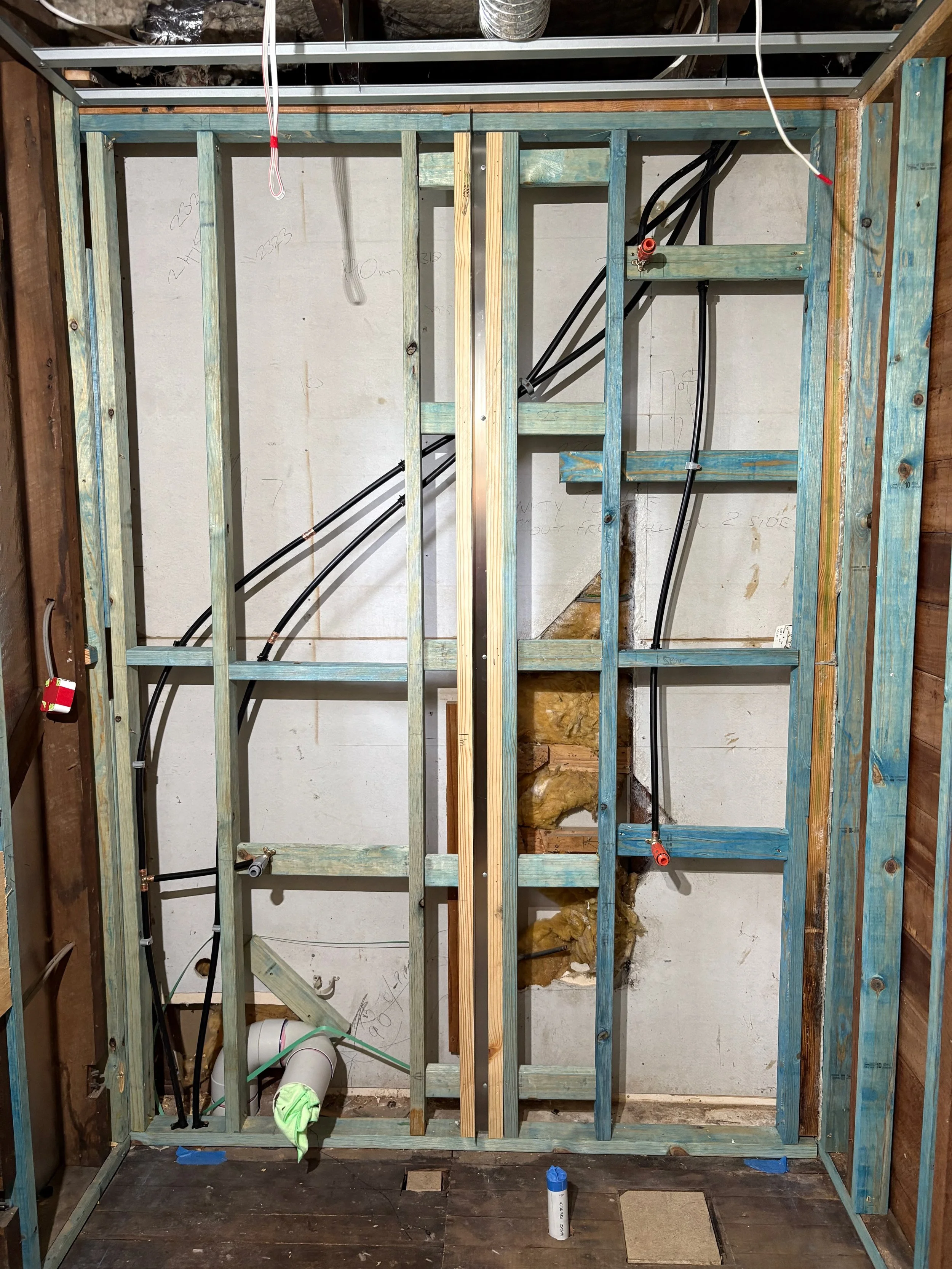 Construction of a wall with electrical wiring and plumbing, with wooden framing and insulation in progress.