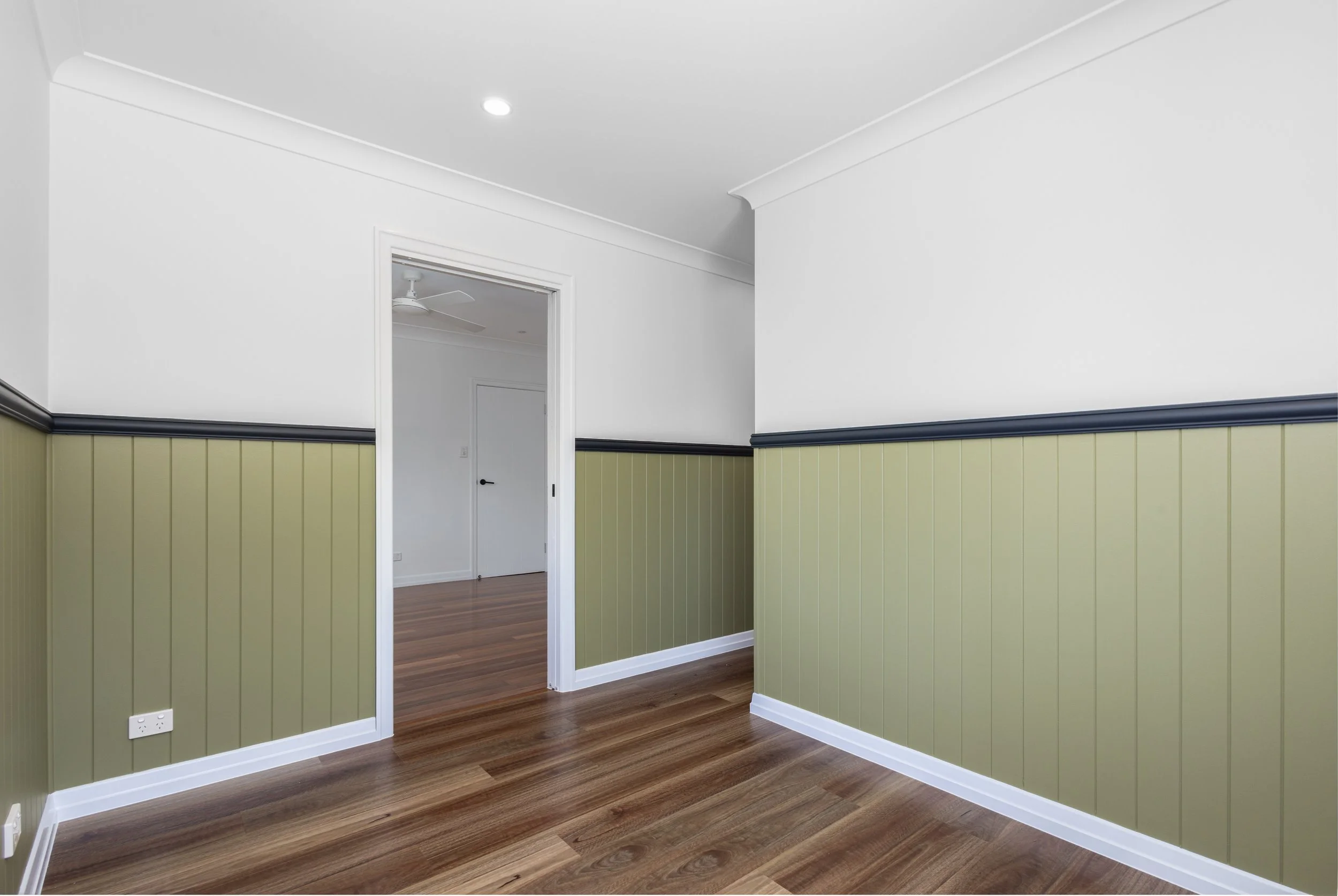 Empty room with white walls, wood flooring, and green wainscoting, doorway leading to another room with similar decor.