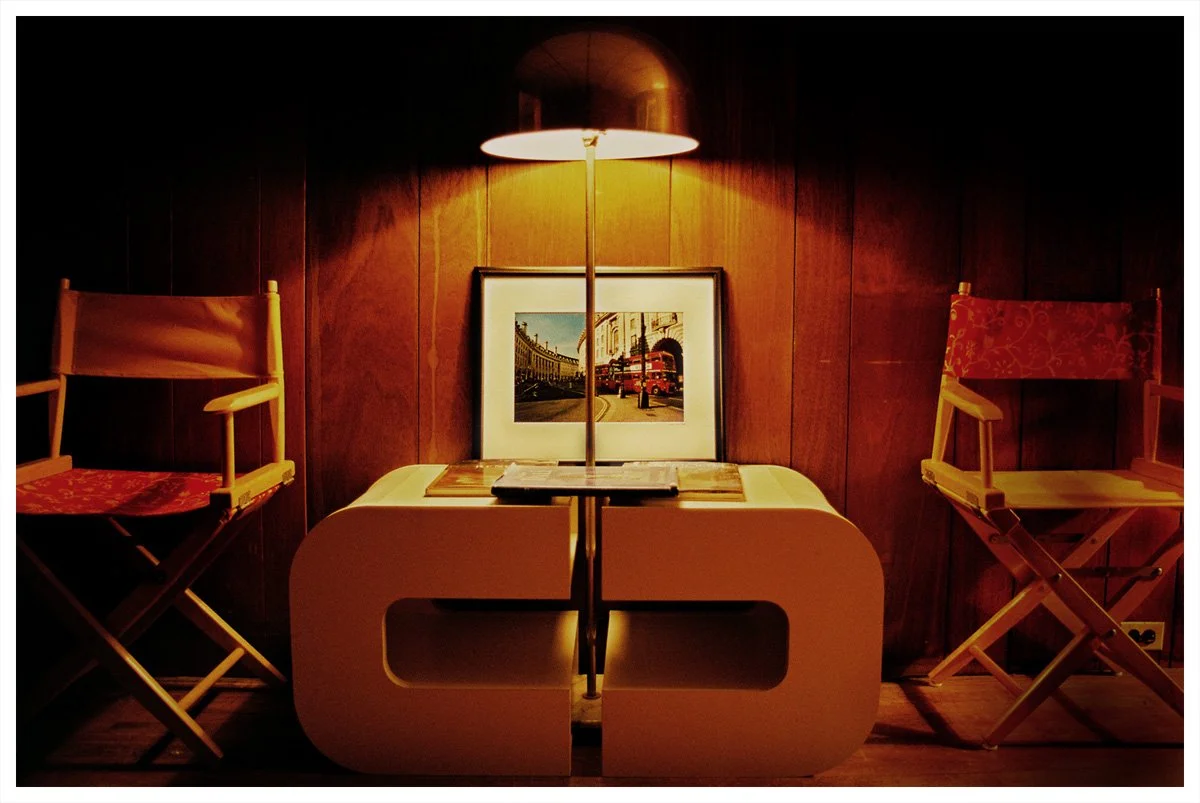 Retro living room with wooden paneling, two director's chairs, a modern coffee table, framed artwork, and a table lamp.