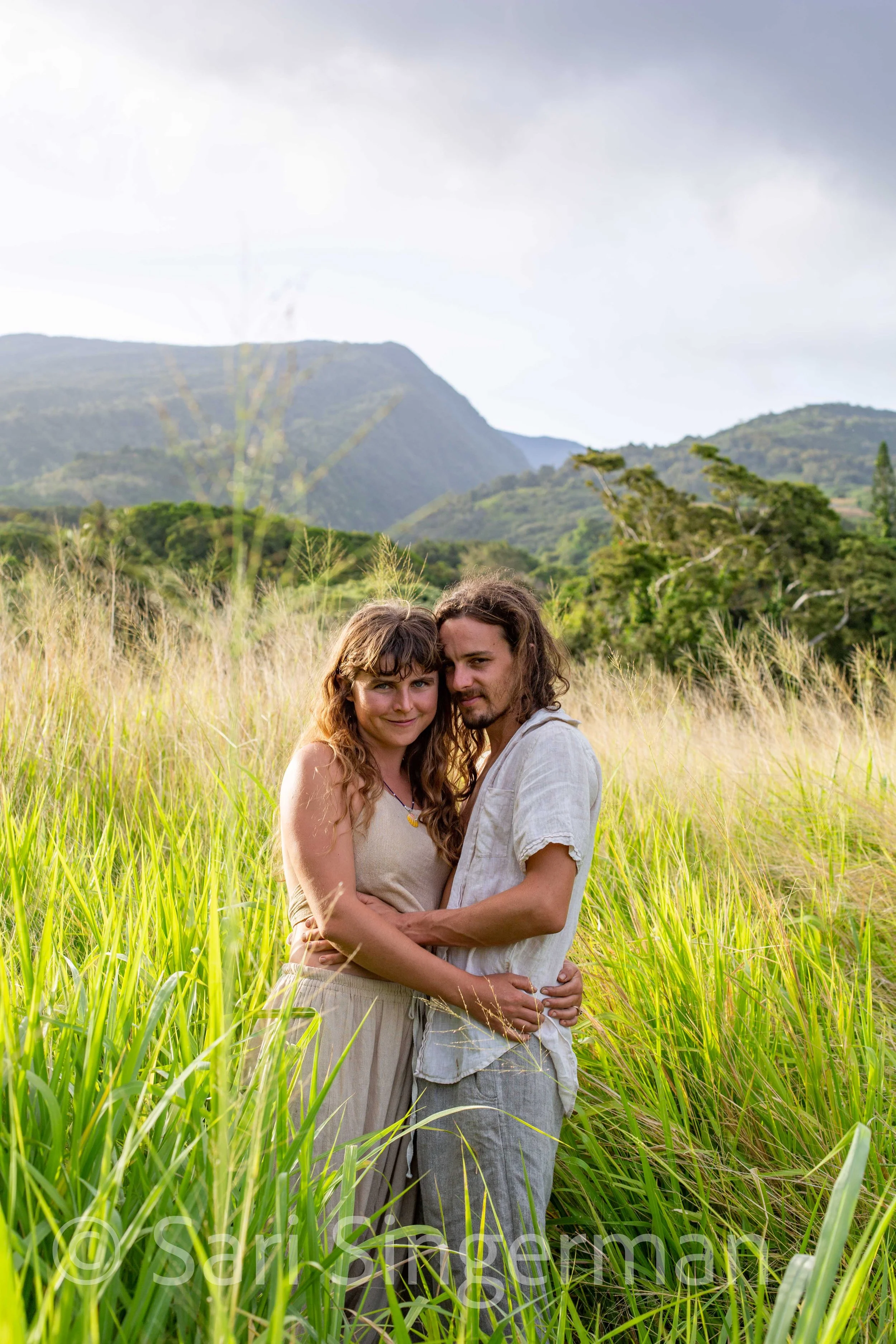 A couple embracing in a grassy field with mountains in the background.