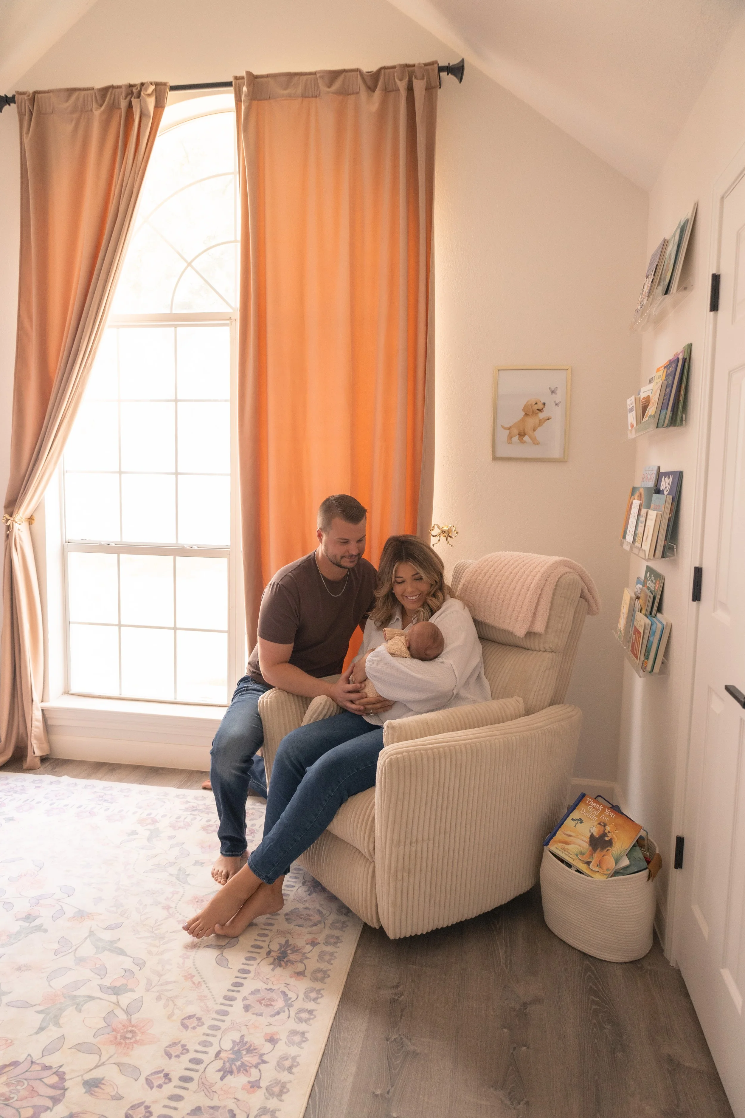 A family celebrating the arrival of a newborn baby in a cozy living room, with a woman holding the baby, a man kneeling beside her, and a smile on everyone's faces.