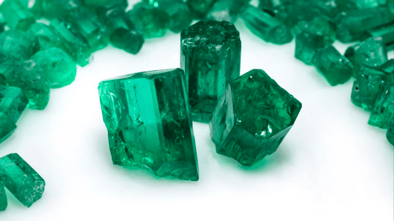 Several rough and polished green crystals, possibly emeralds, arranged on a white surface.