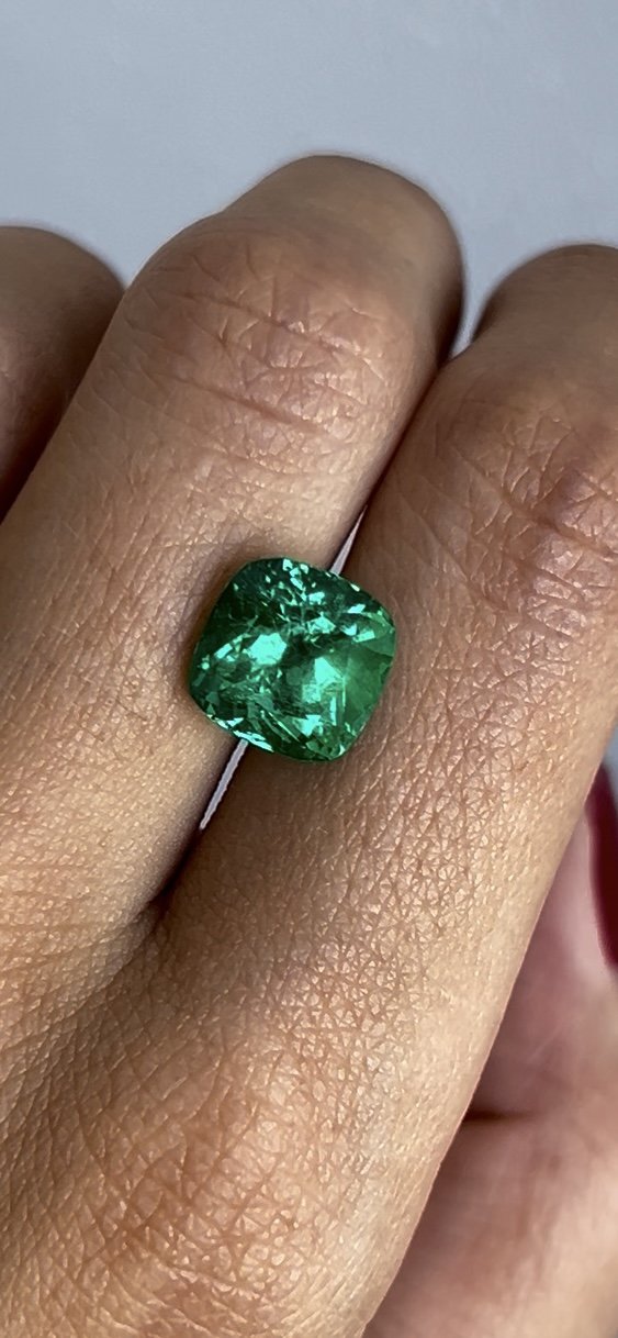 Close-up of a hand wearing a large, emerald green gemstone ring on the middle finger.
