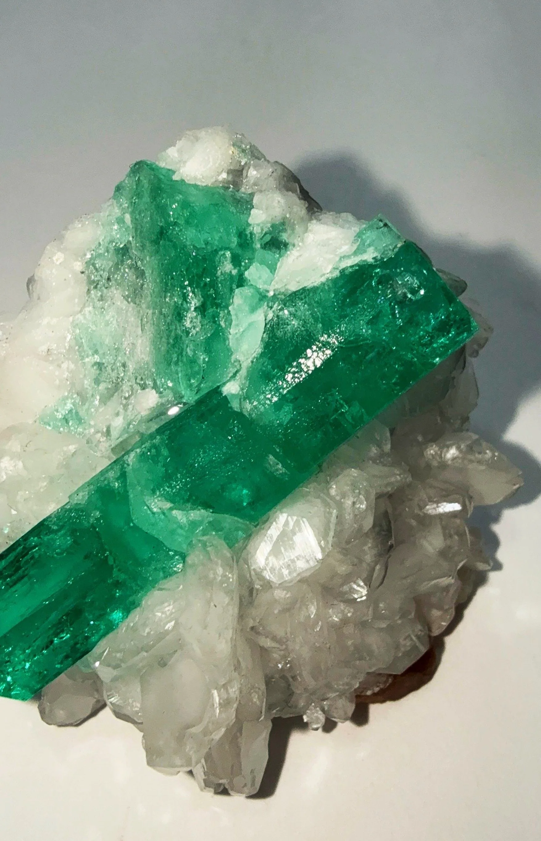 A rough mineral or crystal with green and white sections, sitting on a white surface.