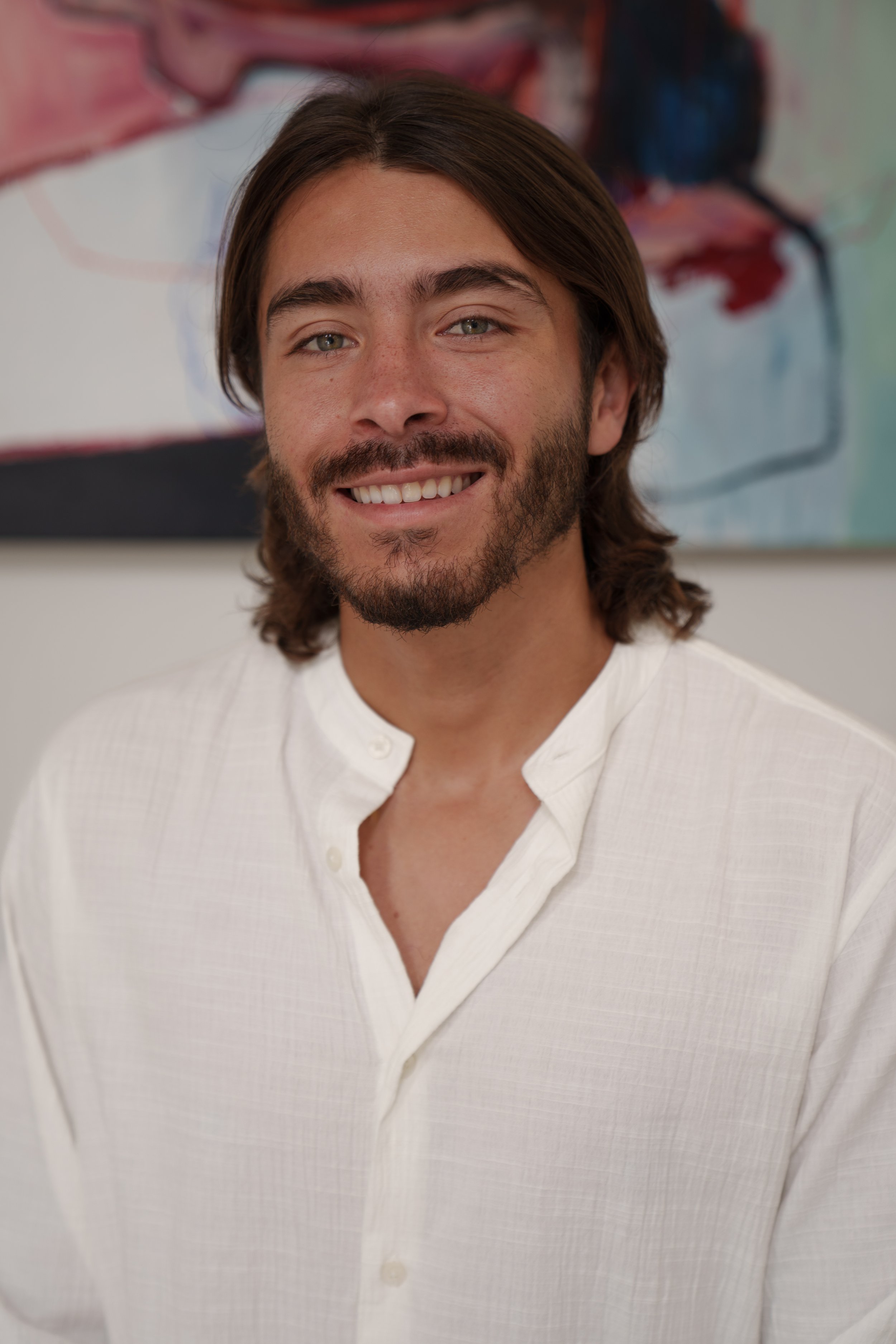 Portrait of smiling man in white shirt in front of abstract art, co-founder of Colombian Gems.