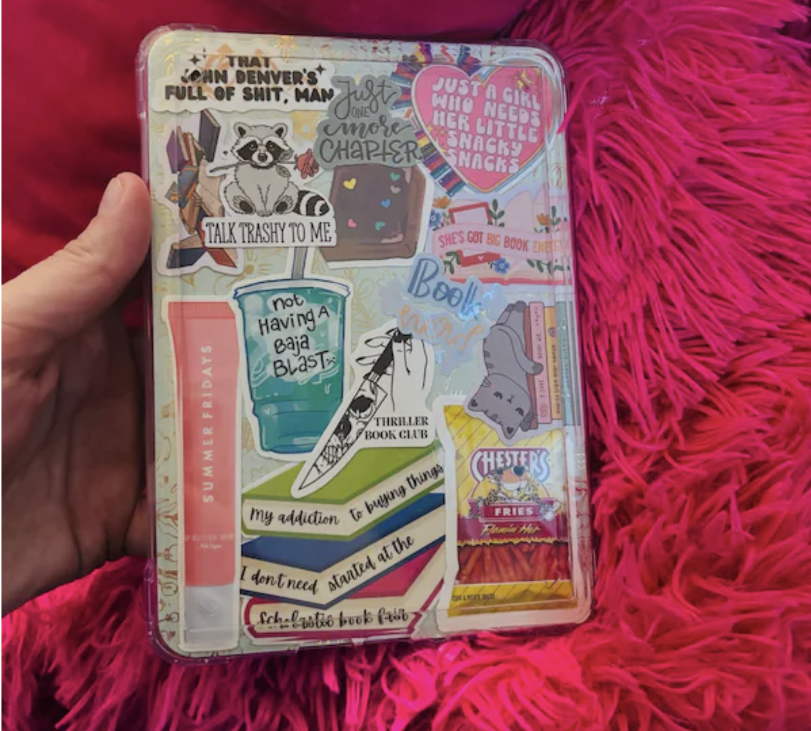A transparent plastic container filled with various colorful stickers, some featuring humorous or playful phrases, animals, books, and snacks.