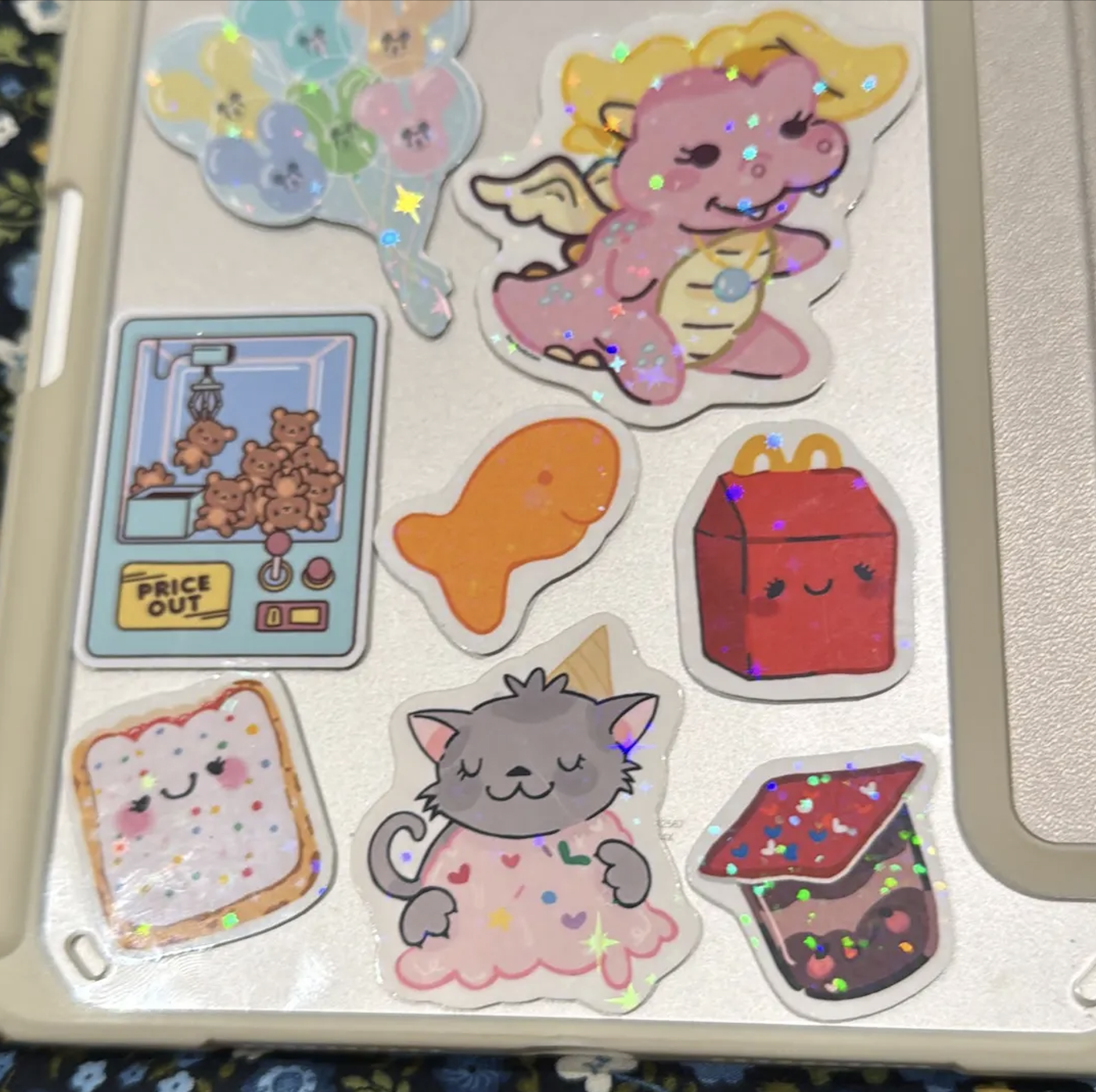 Collection of colorful stickers on a laptop, including a unicorn, teddy bears in a claw machine, an orange fish, a red Happy Meal box, a slice of bread with a smiling face, a gray cat with hearts and stars, and a boba tea cup with a smiling face.