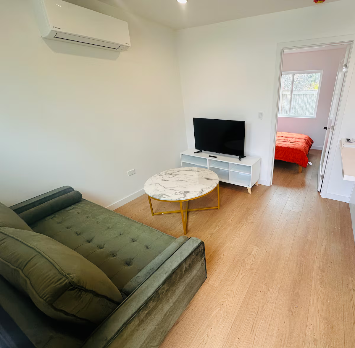 Modern living room with a green sofa, marble coffee table, flat-screen TV on a white console, and wood flooring.