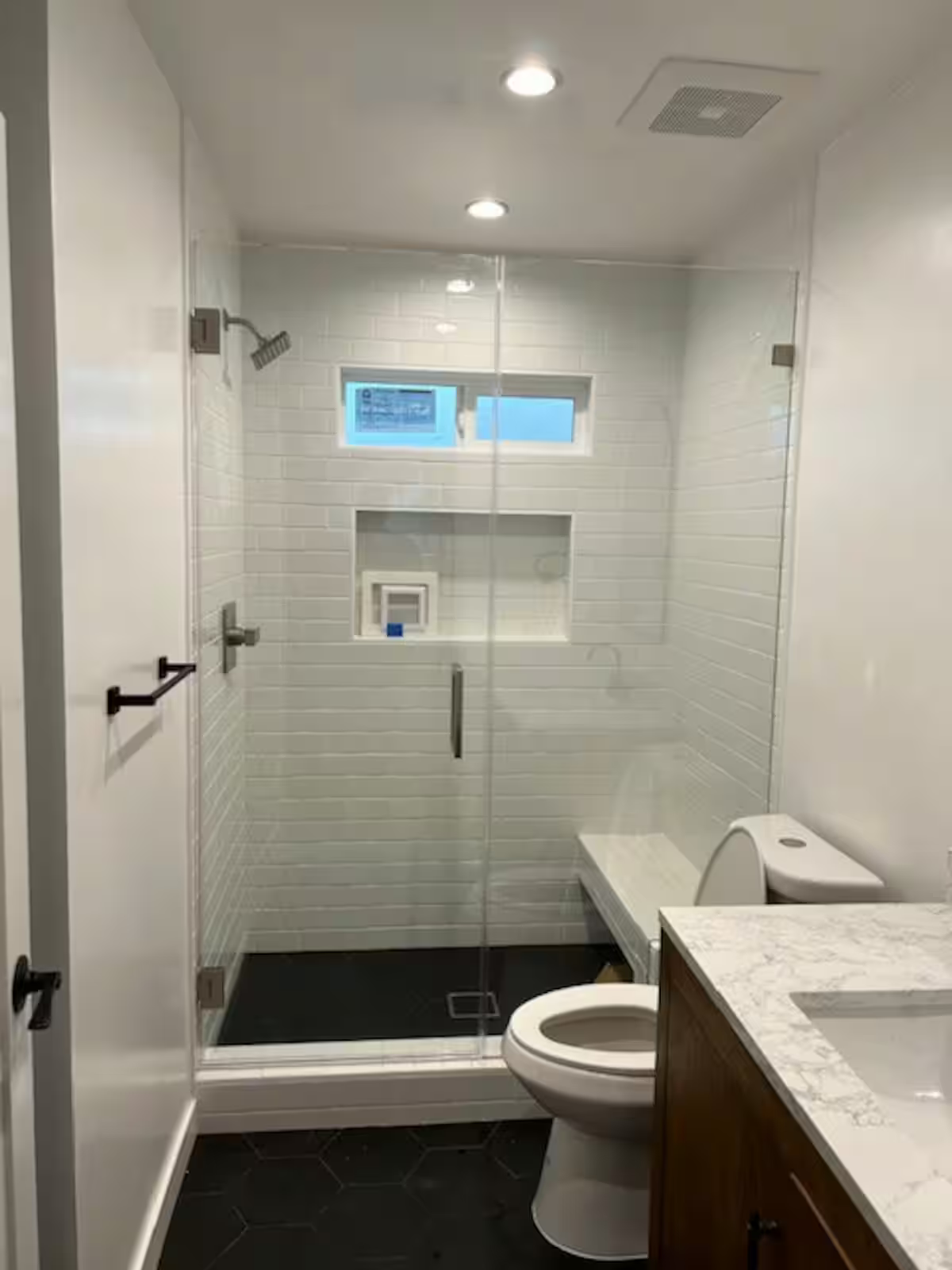 Modern bathroom with glass shower, white subway tiles, toilet, and marble countertop.