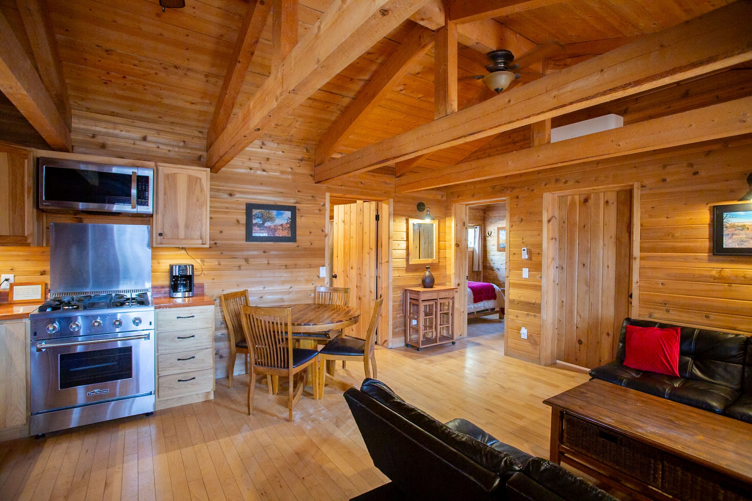 Interior of a wooden cabin with a kitchen area and sitting area, wooden ceiling beams, and framed pictures on the wall.