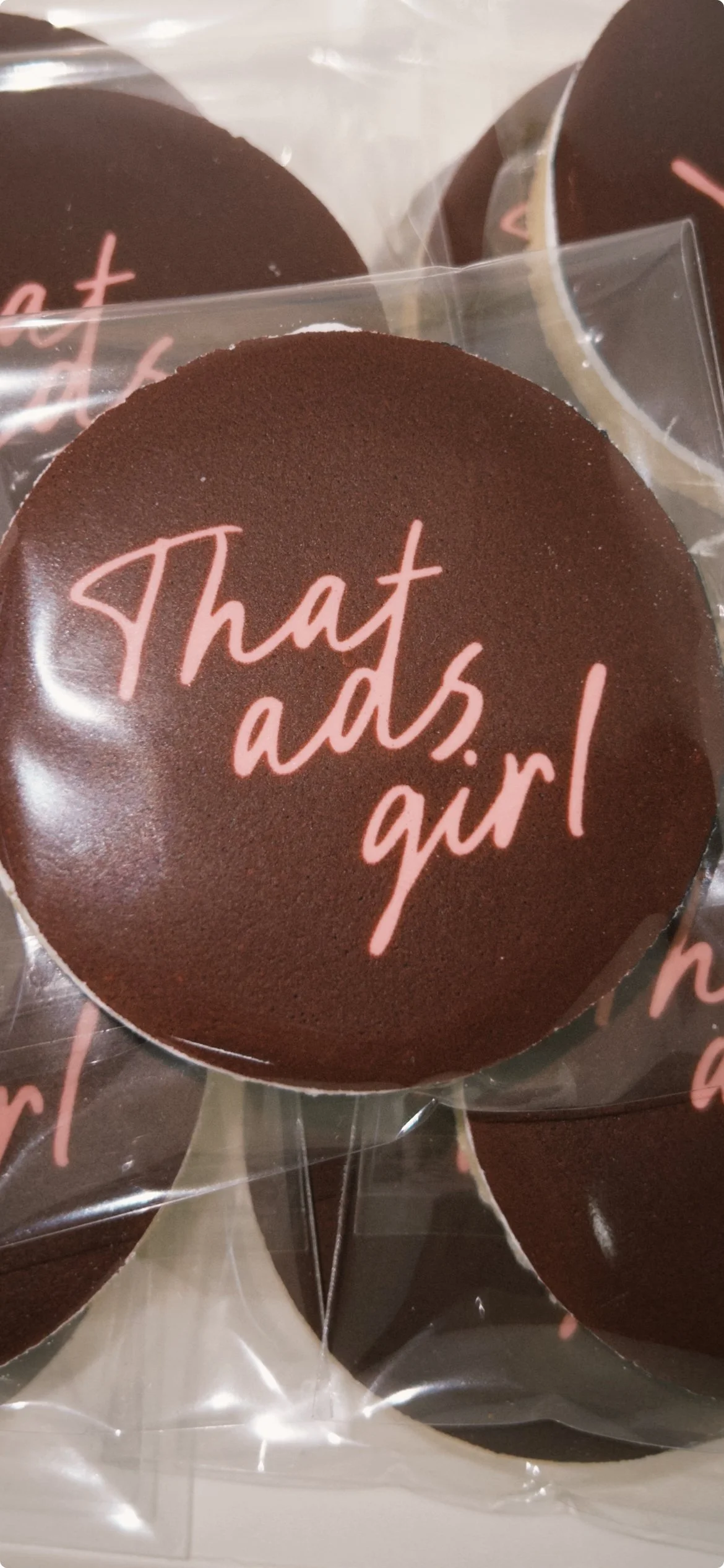 A round chocolate cookie with pink cursive text that reads "That ads, girl" in plastic wrapping.