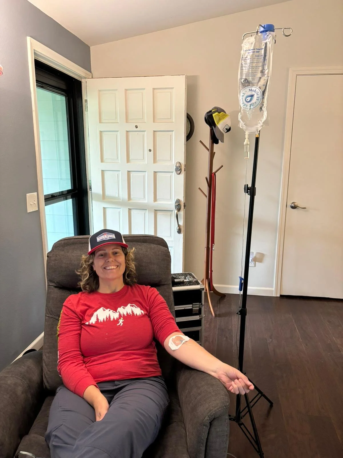 A woman smiling in a recliner, with an mobile IV in her arm, representing a wellness IV therapy service from the IV menu offerings.