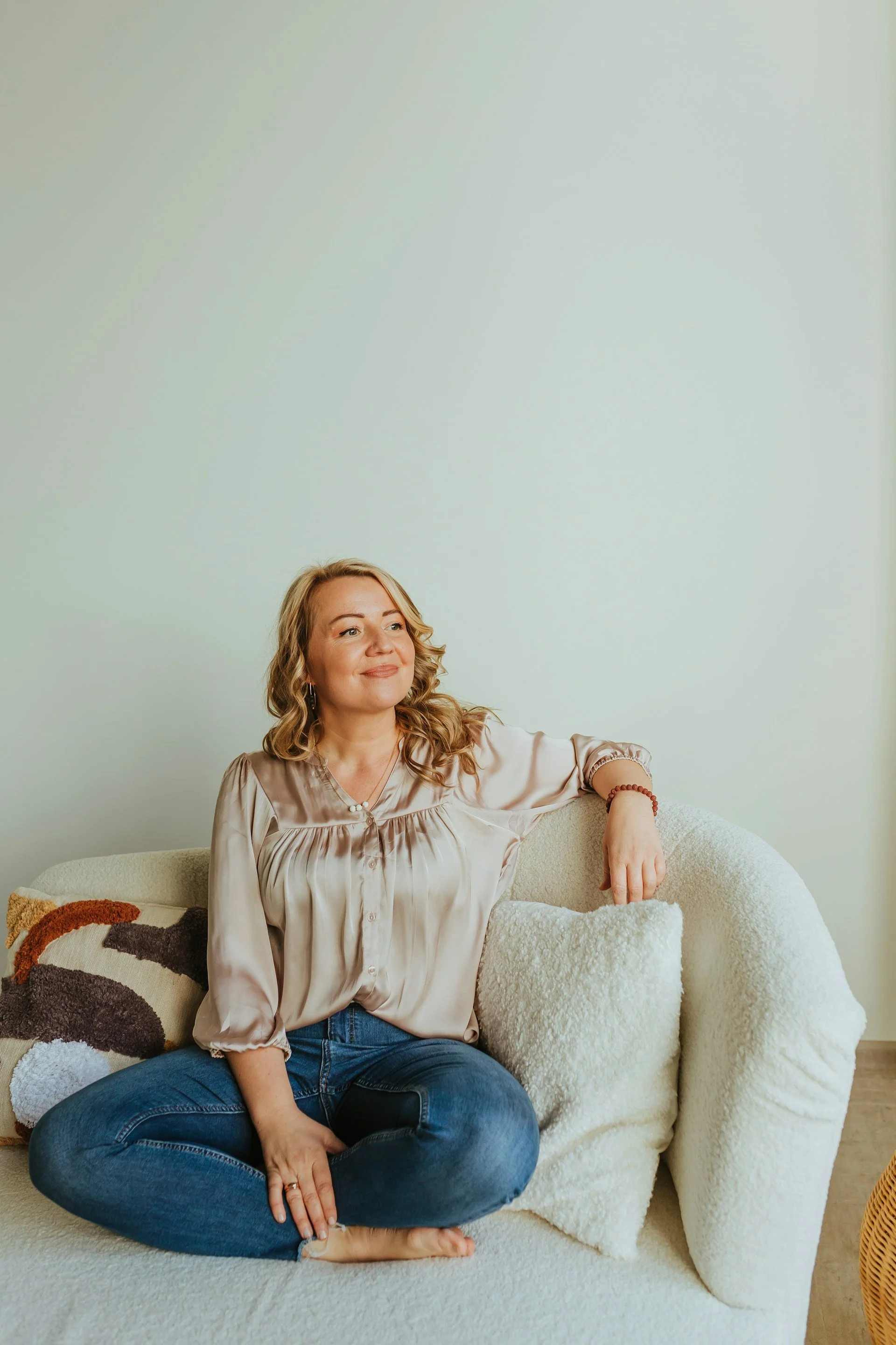A woman smiles while sitting on a chair with pillows, representing the ease of at home botox and microneedling services.