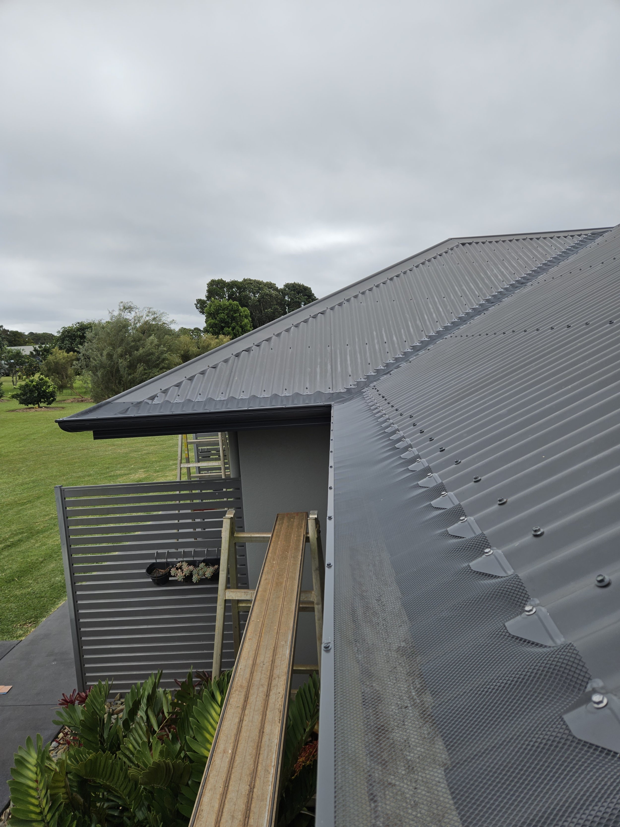 Close-up view of a metal roof on a building with new Gutter guard installed, with a cloudy sky and greenery in the background.