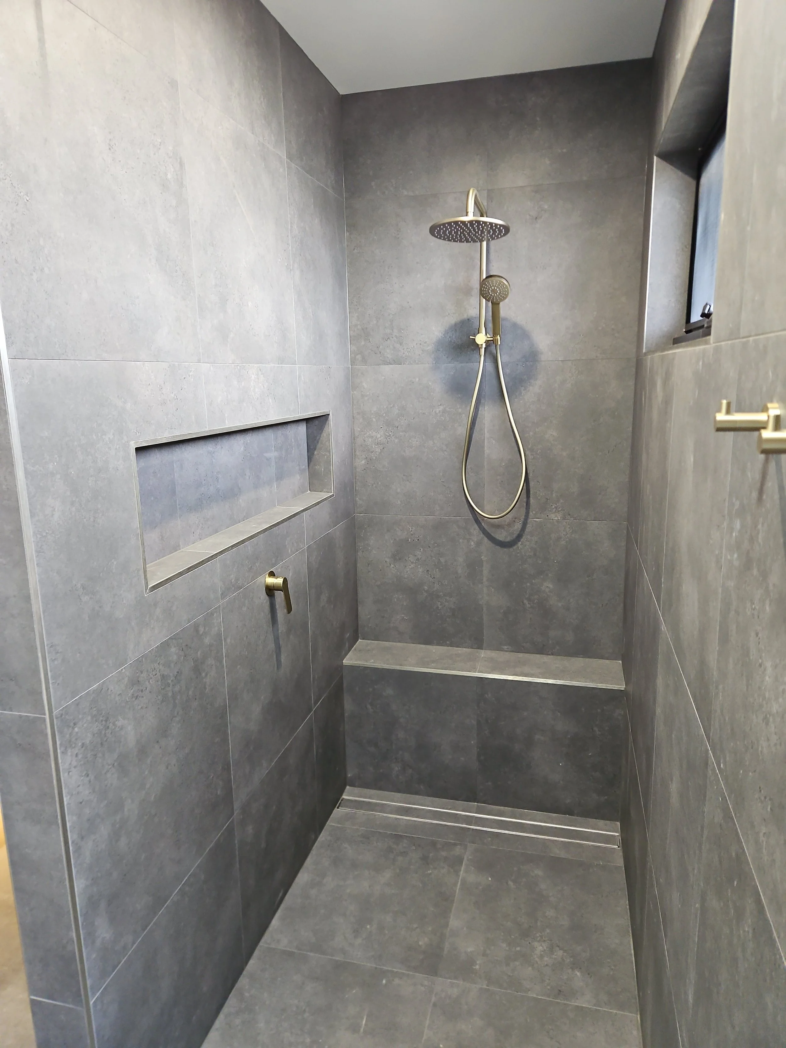 Modern gray-tiled shower with built-in niche, brass fixtures, and rain showerhead.