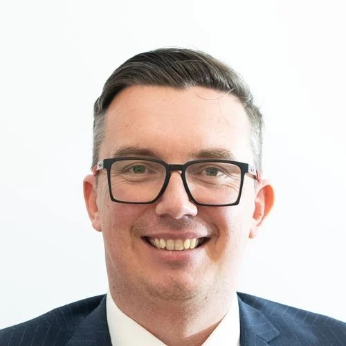Profile photo of William Whitby with glasses smiling in front of a white background.