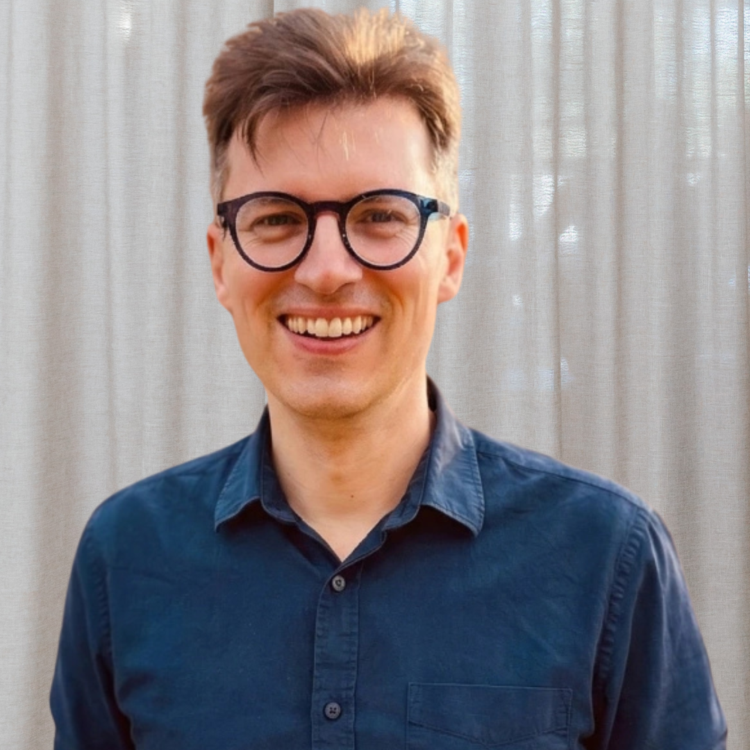 person wearing blue button up shirt and black rimmed glasses smiling