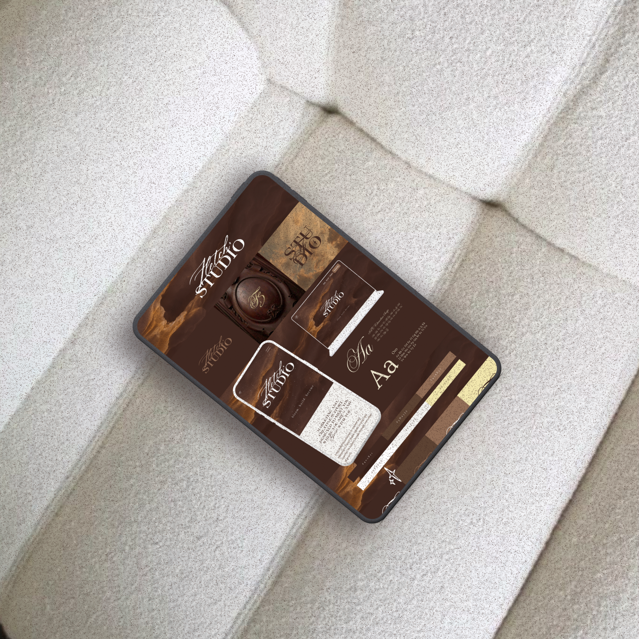 A mock up of a smartphone lying on a white textured surface displaying a dark brown themed design with text in cursive and serif fonts, possibly related to a studio or creative branding, with design elements and color swatches.