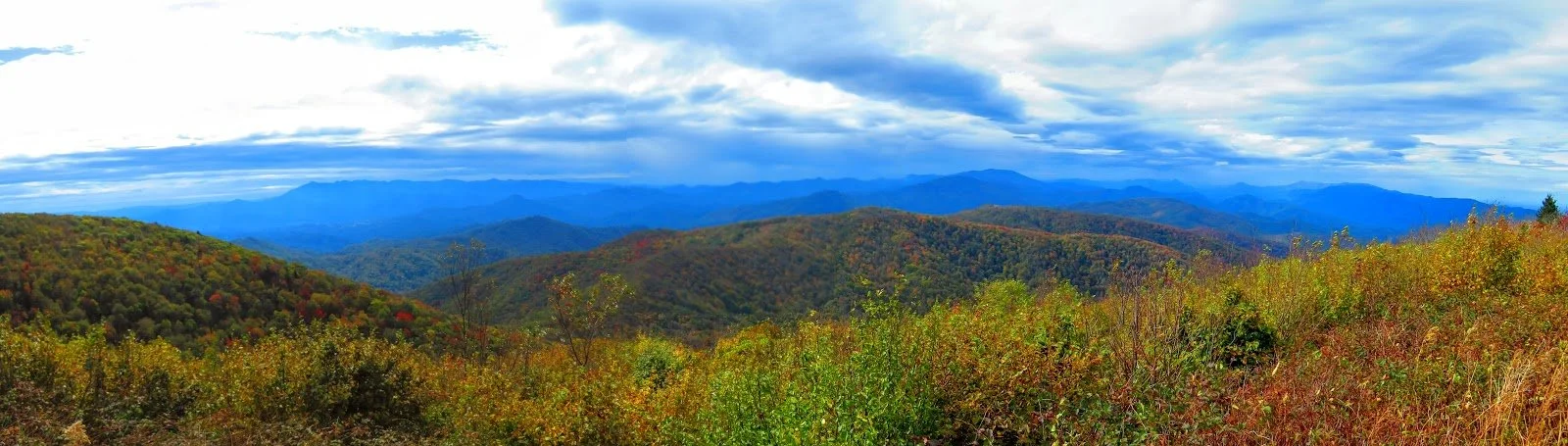 Panoramic view of the Great Smoky Mountains with colorful autumn foliage and a cloudy sky.