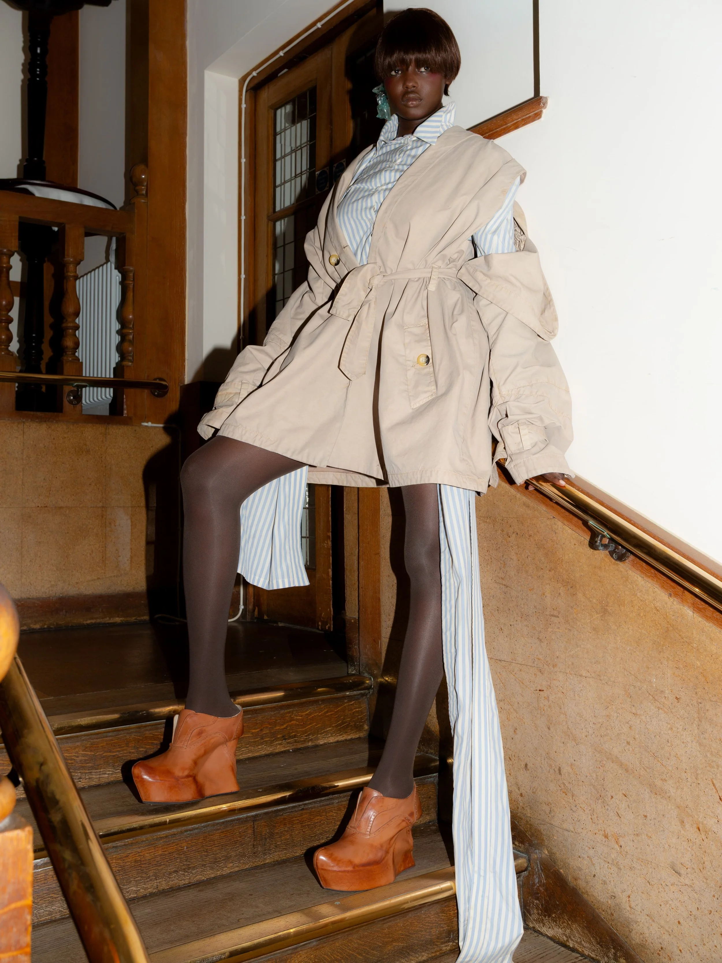 Model wearing a deconstructed beige trench, striped trousers, platform shoes and Tétier Bijoux jewellery at the Masha Popova AW26 show.