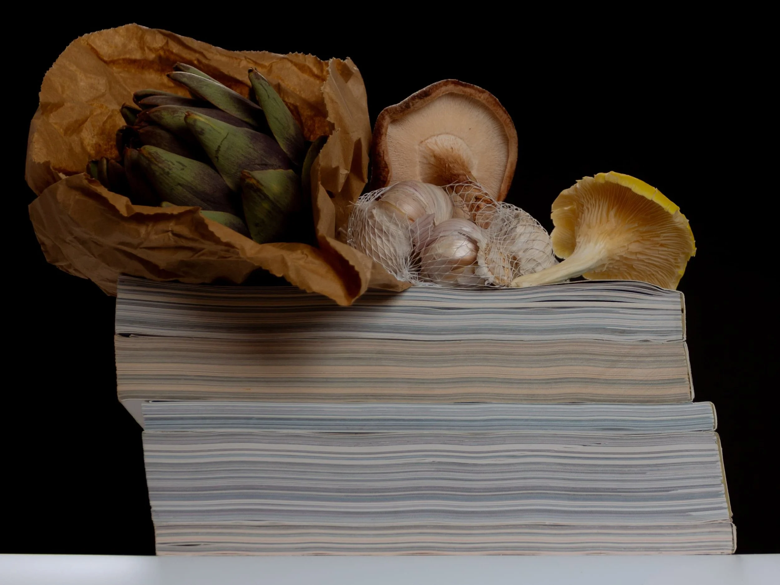Still life photograph featuring artichokes, mushrooms, garlic and stacked books by Yaroslav Prytula, still life photographer based in Manchester and working in London.