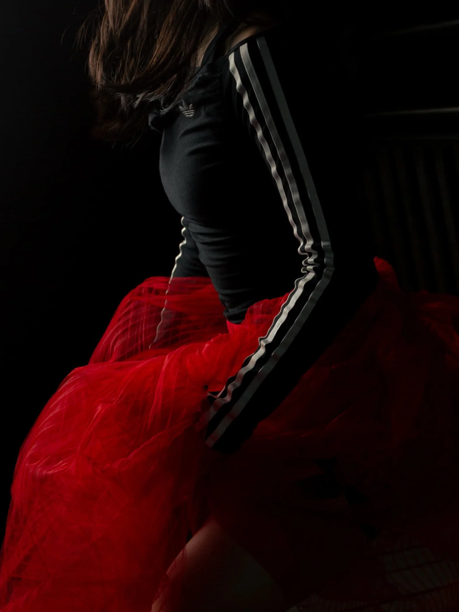 Woman wearing an adidas tracksuit with a red skirt in a dark, low-lit setting, photographed by Manchester and London based photographer Yaroslav Prytula as a supporting image for the film Sonata for Common Frequency.