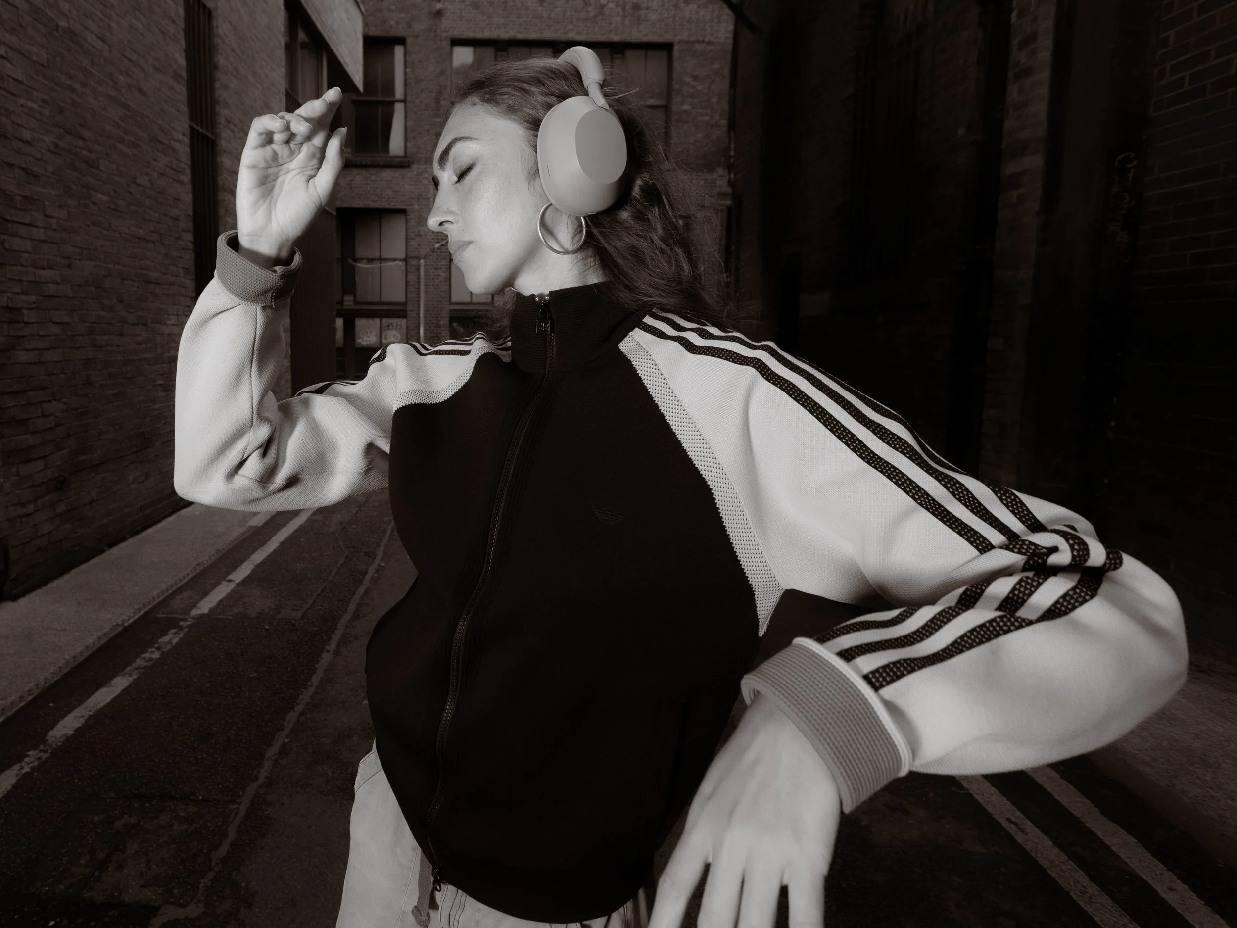 Black and white portrait of a woman dancing in an adidas tracksuit and headphones in an industrial Manchester setting, photographed by Manchester and London based photographer Yaroslav Prytula for Common Frequency.
