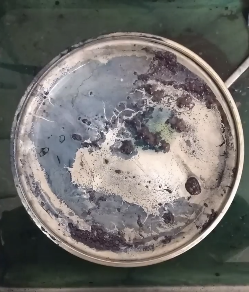 Close-up of a worn and dirty metal paint can lid with indigo and black and beige paint splatters and residue.
