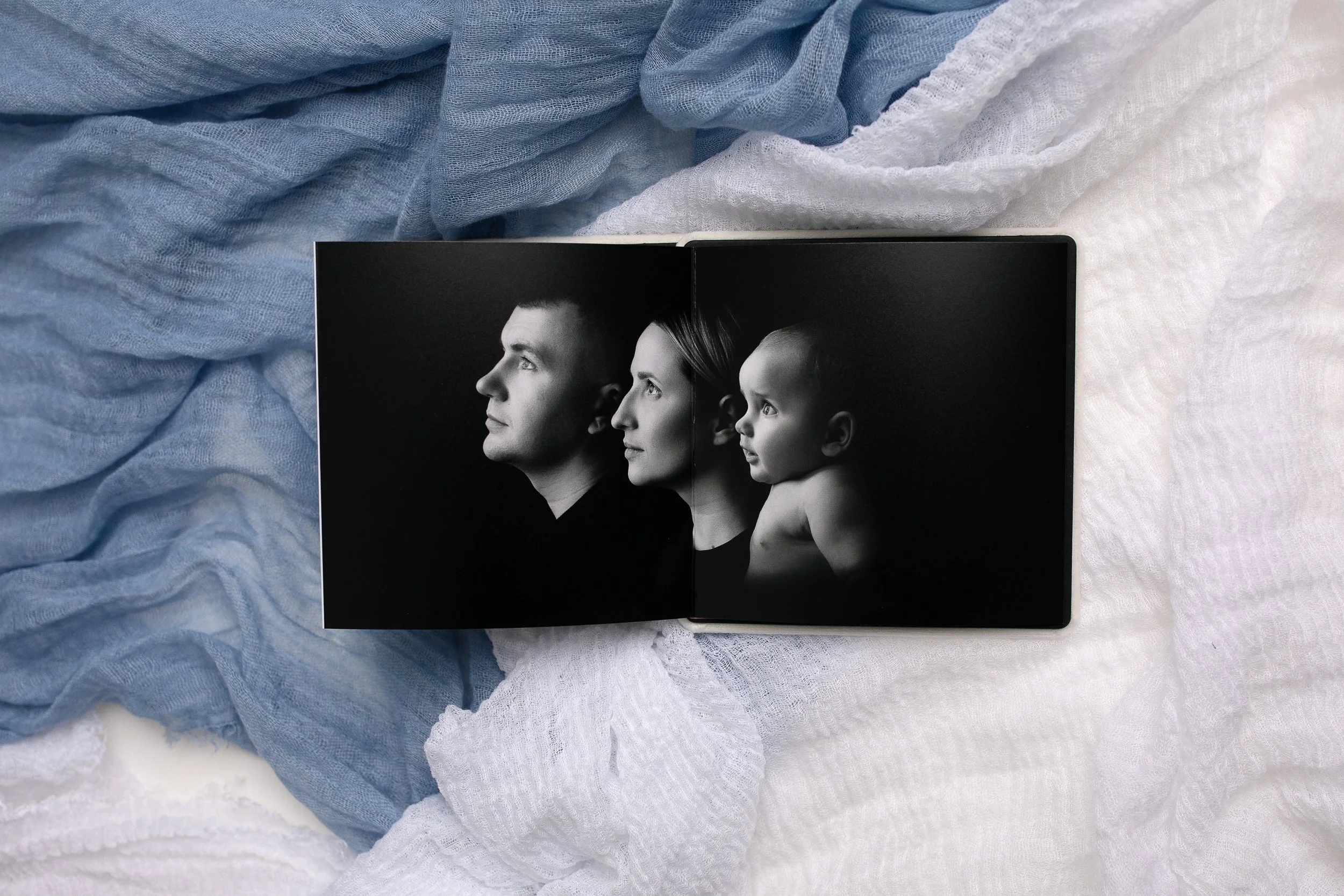 Color photograph of a family  including a mother, father, and one baby boy, posed together and smiling. The photo is black and white. This is the generation portrait