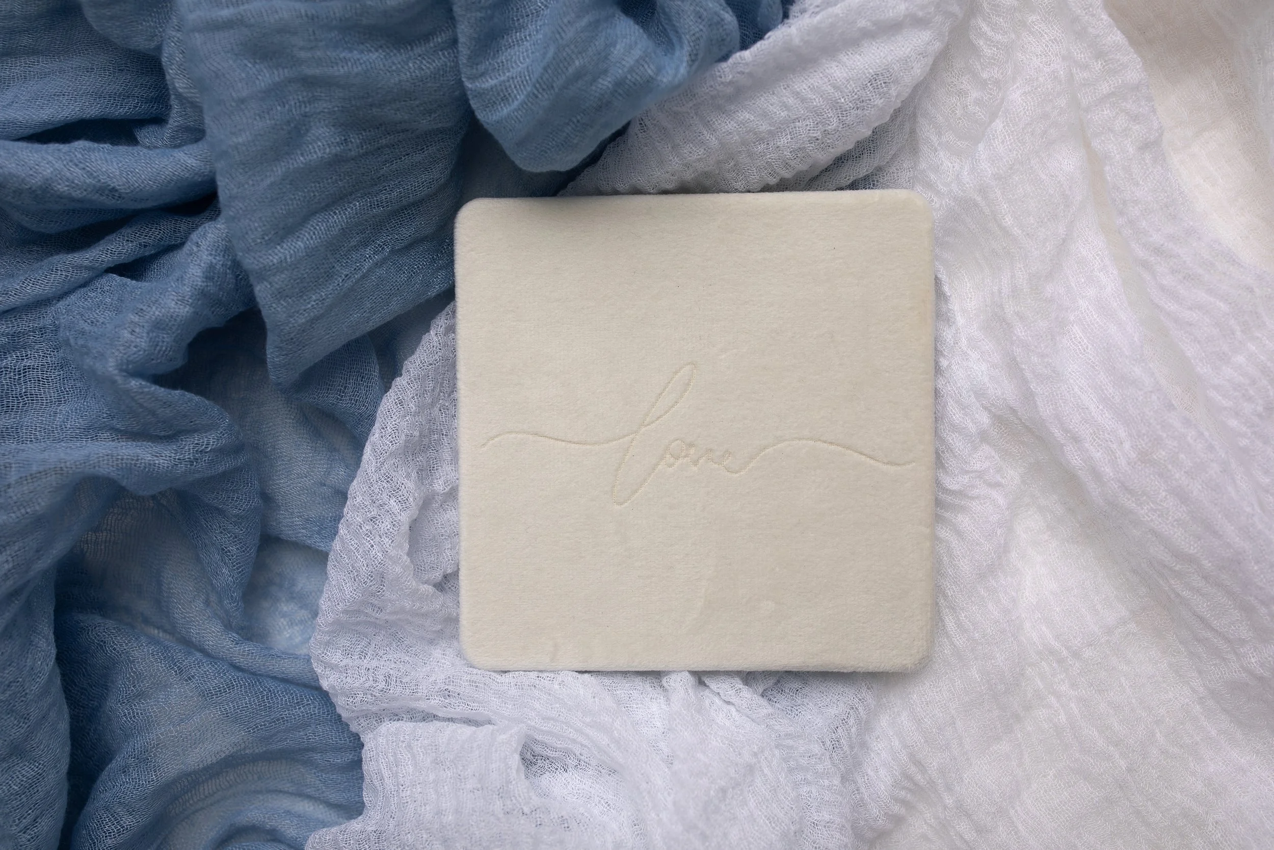 A small white album placed on soft, blue and white fabric.