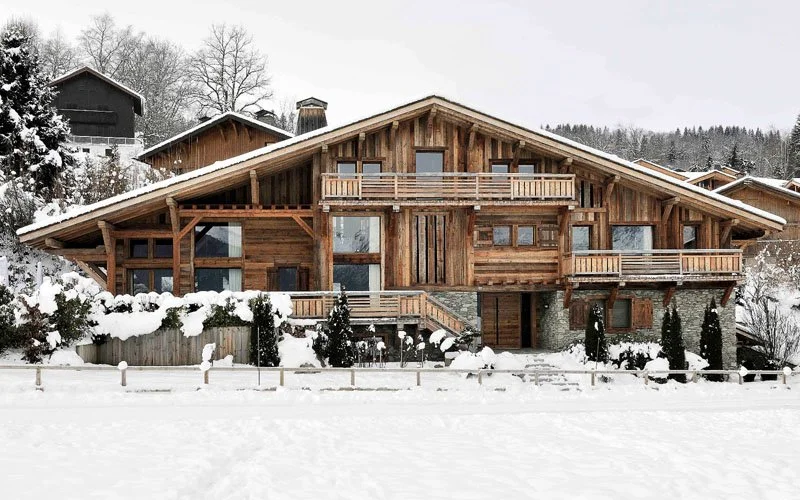Large wooden chalet-style house in a snowy landscape surrounded by trees and neighboring houses.